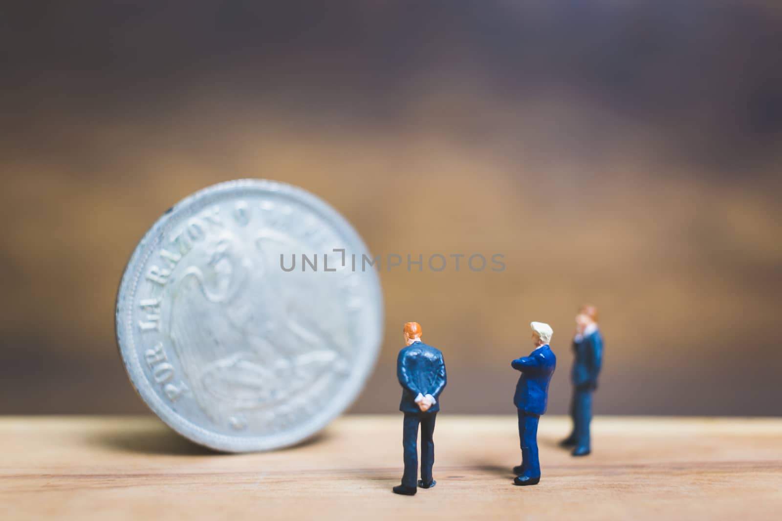 Miniature people : Businessman standing near coin with wooden background : Business concept.