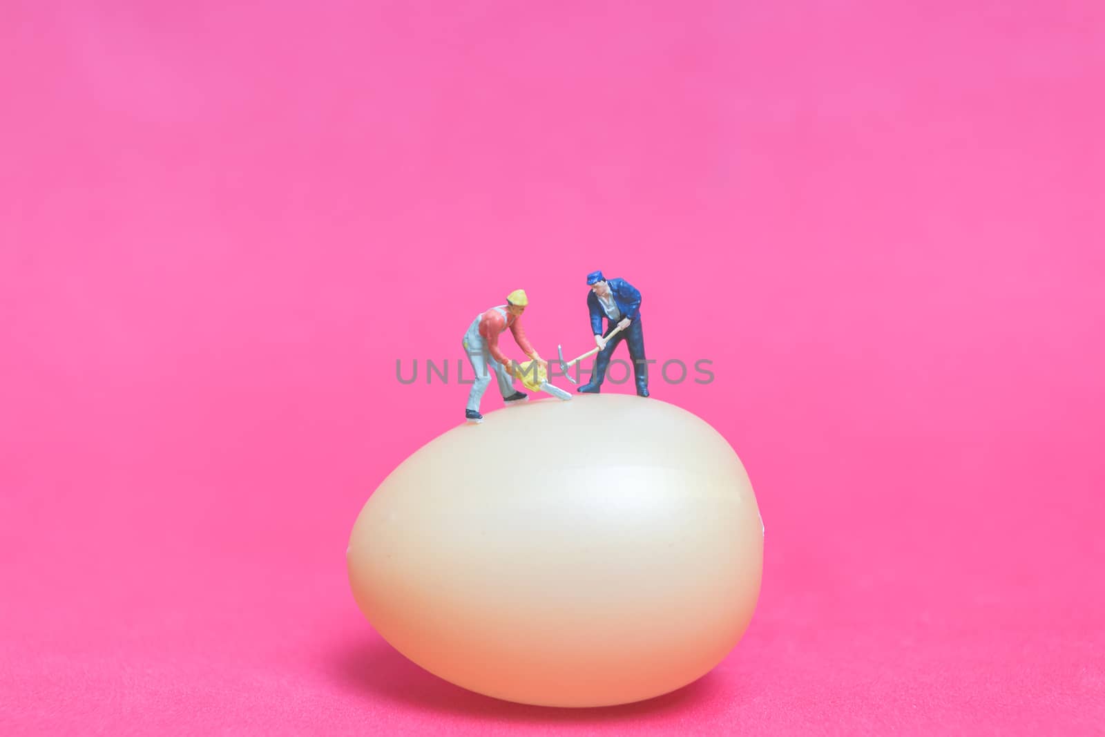 Miniature people work at Easter-eggs for Easter day on pink background