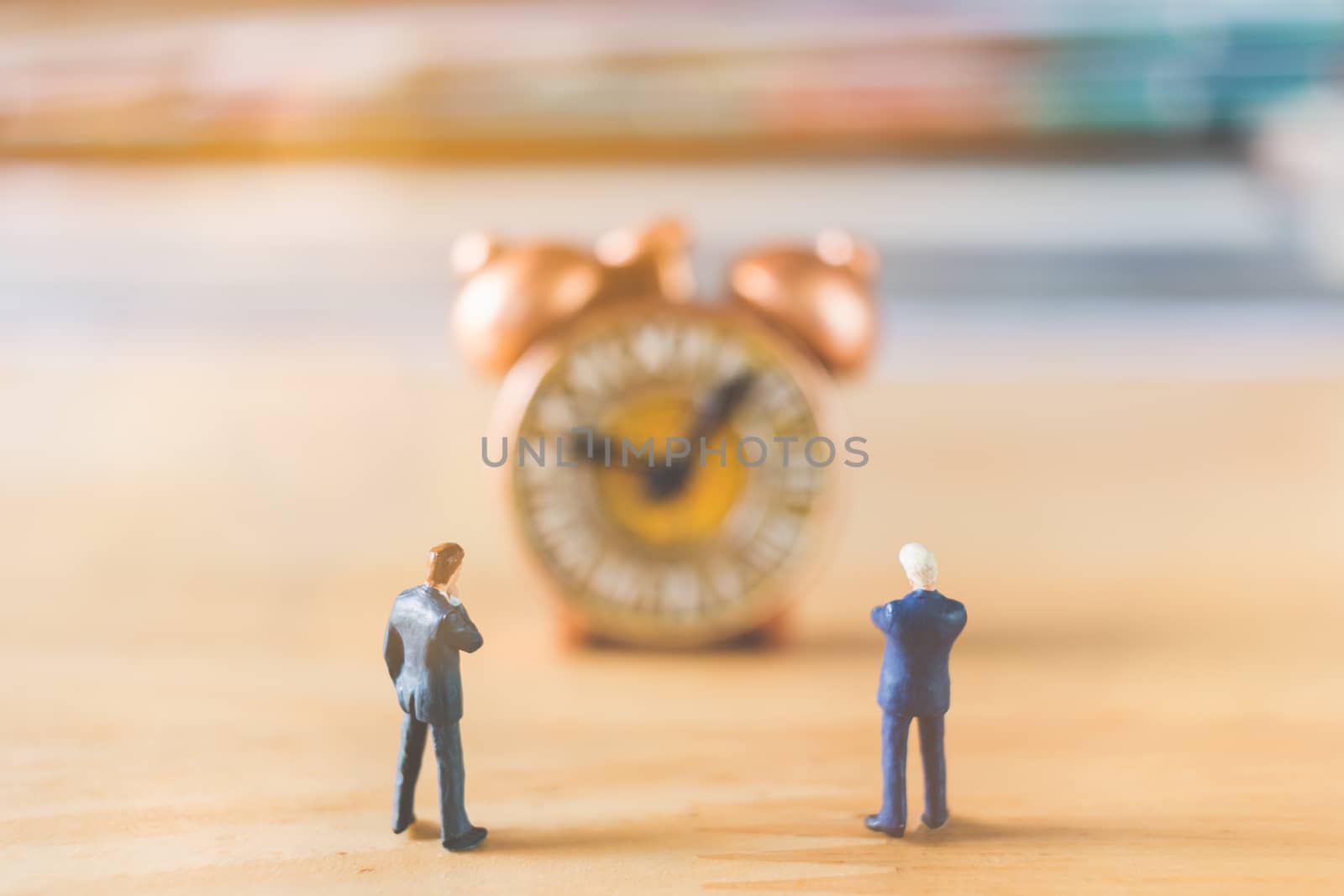 Miniature people: Businessman standing with Ancient clock on wooden background