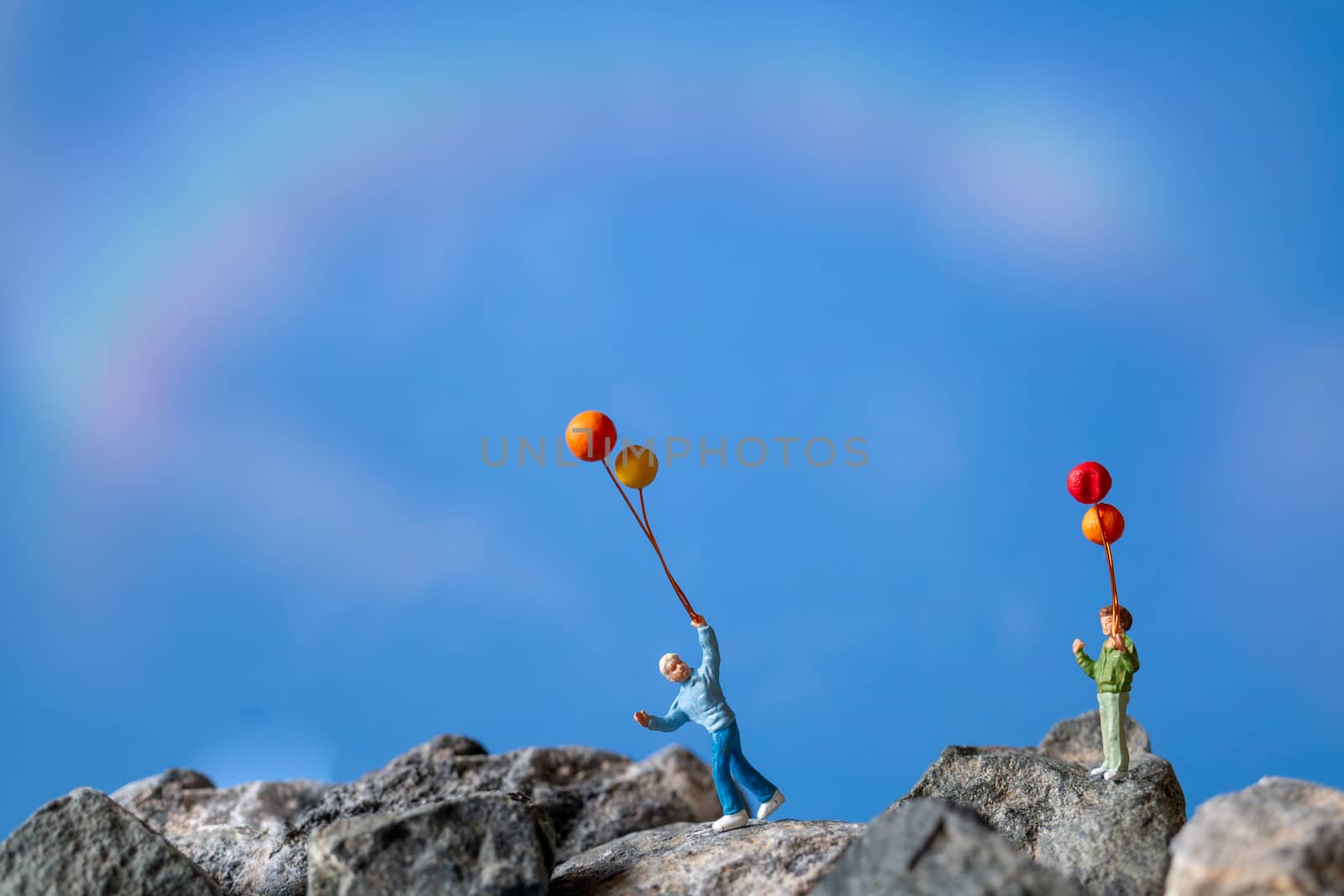 Miniature people , Happy family holding balloon on The rock with blue sky background