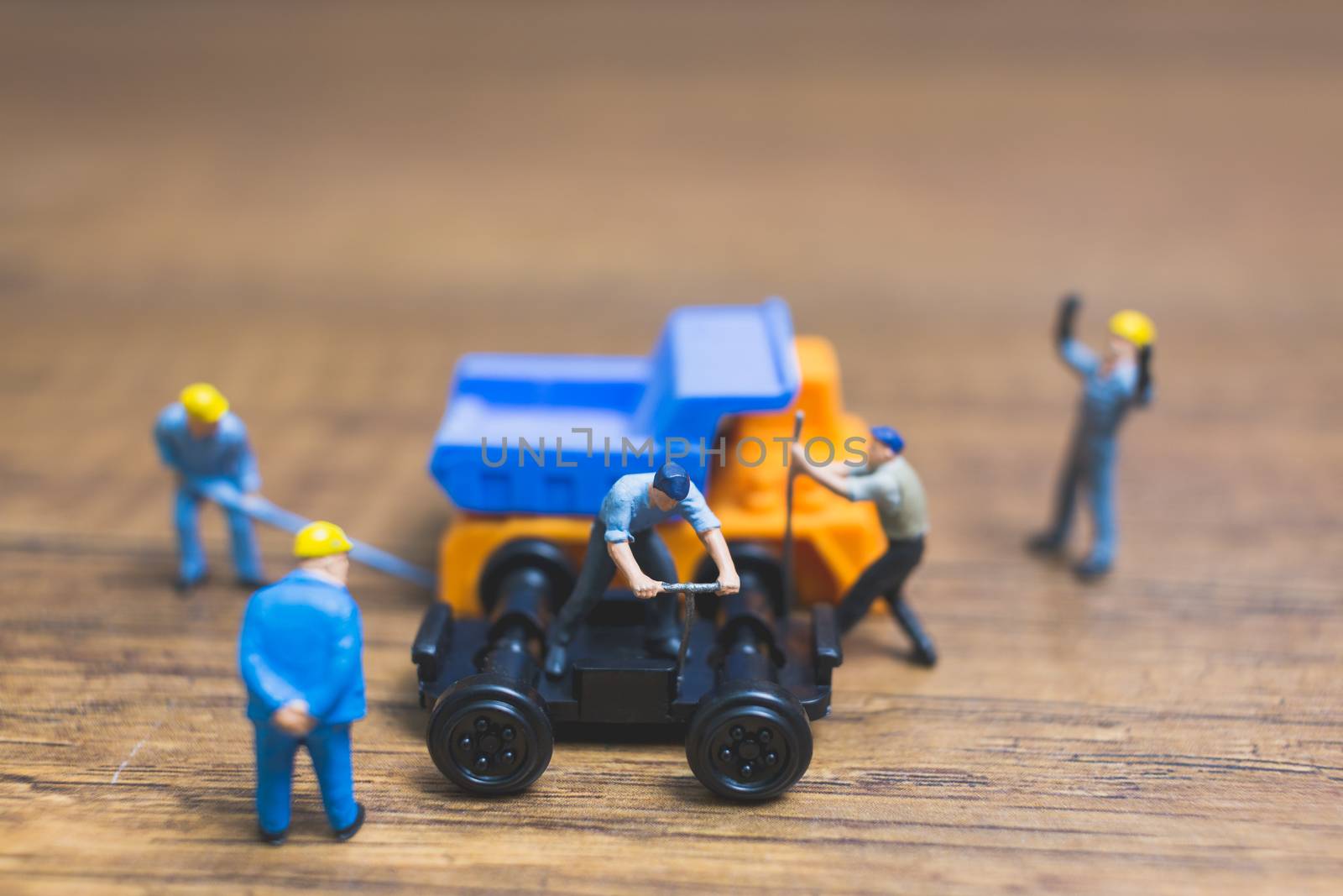 Miniature people : Worker repairing wheel of a truck on wooden background