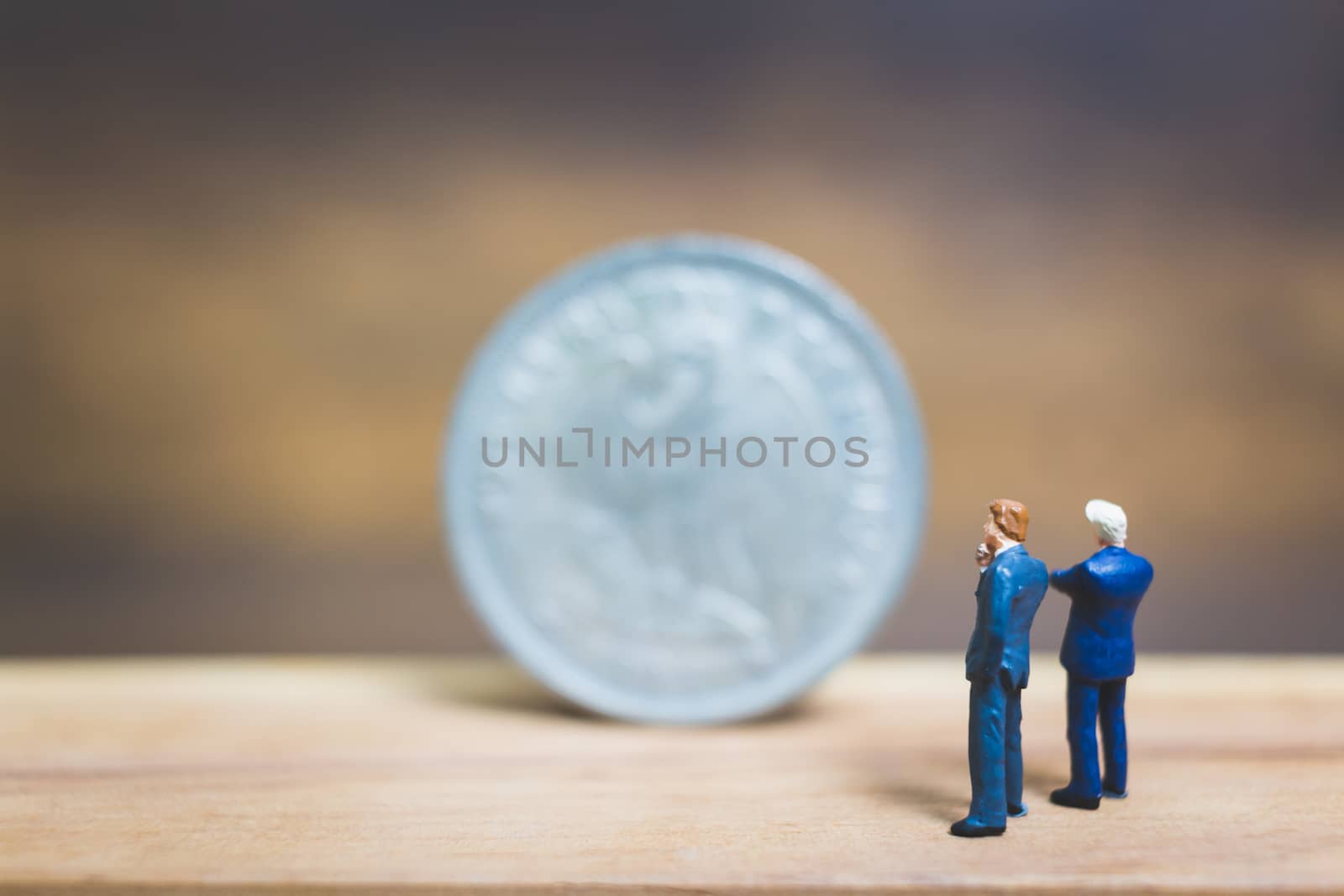 Miniature people : Businessman standing near coin with wooden background : Business concept.