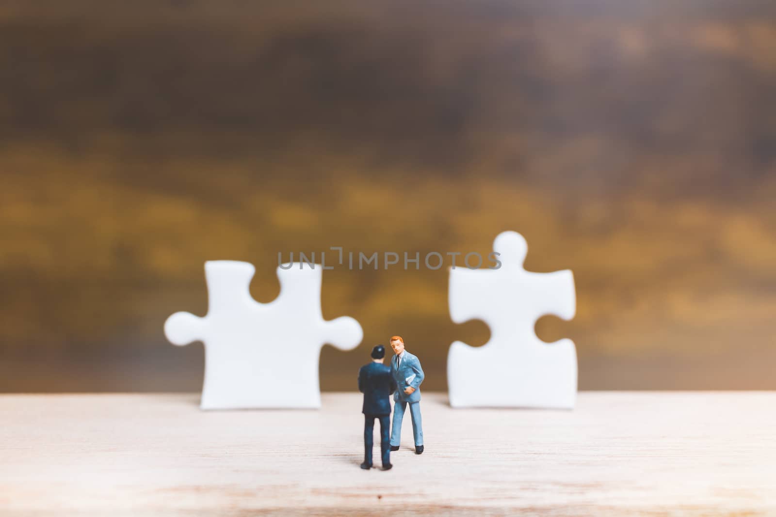 Miniature people: Businessman standing on jigsaw with wooden background : Business concept.