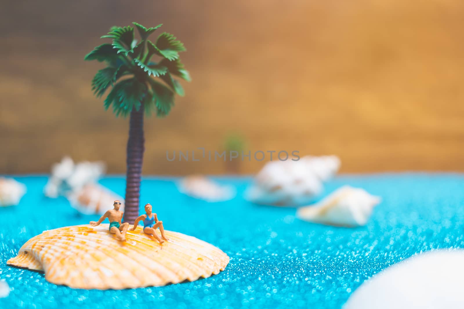 Miniature people wearing swimsuit relaxing on a seashell with blue glitter background