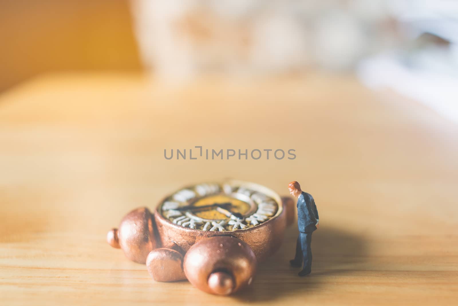 Miniature people: Businessman standing with Ancient clock on wooden background