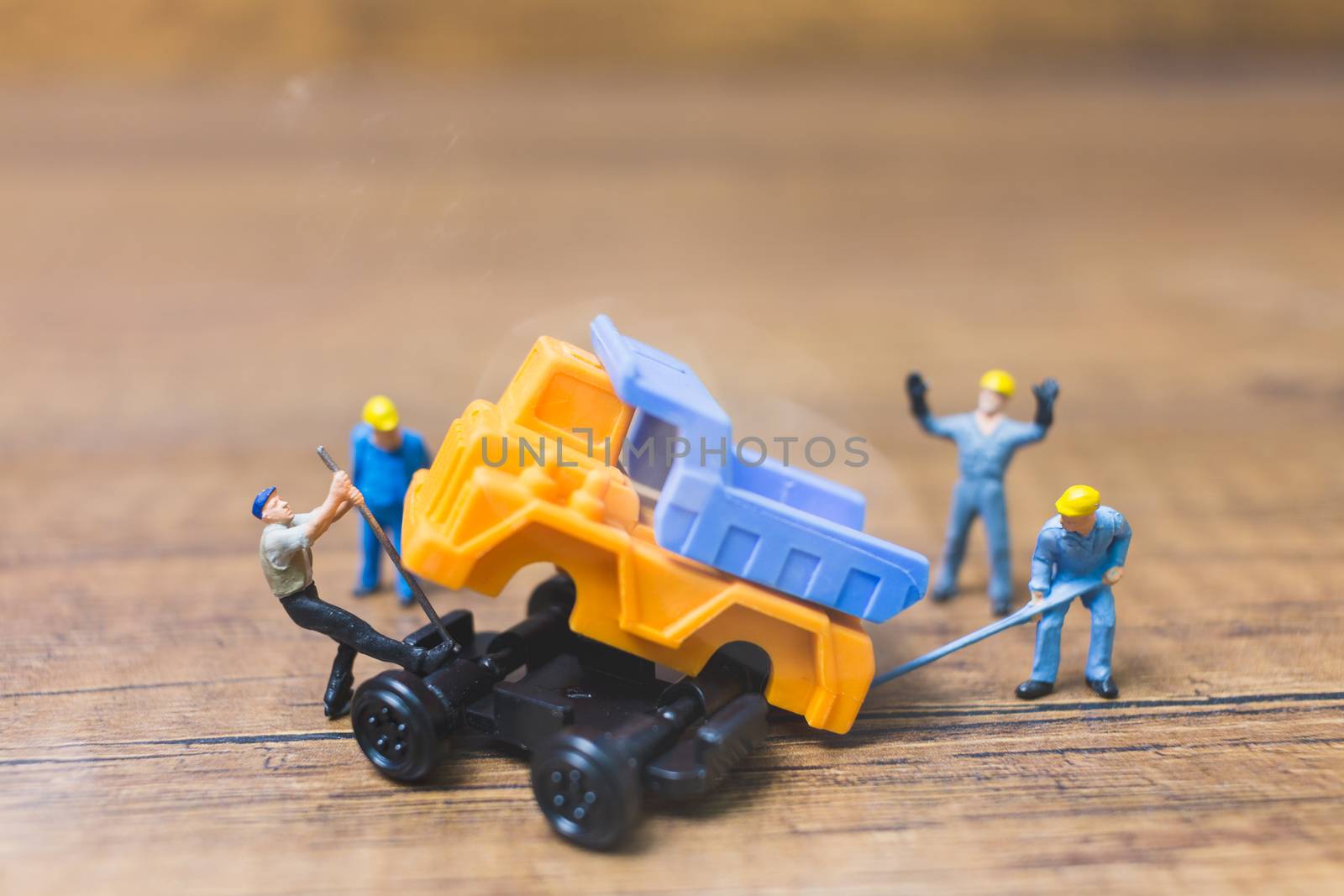 Miniature people : Worker repairing wheel of a truck on wooden background