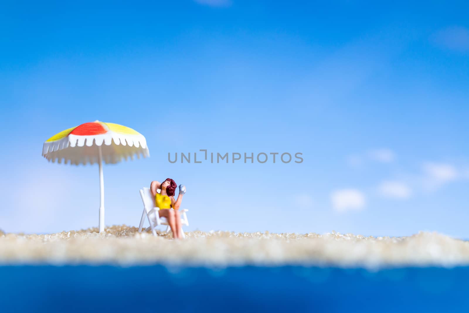 Miniature people sunbathing on The beach with blue sky background , Summer time concept