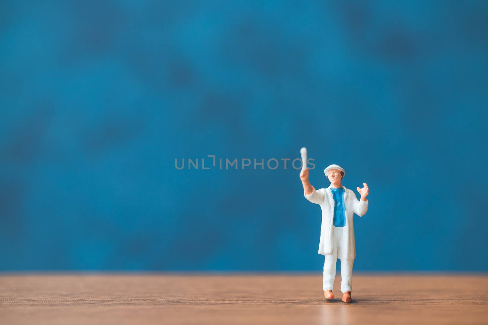 Miniature people holding brush in front of a blue wall background