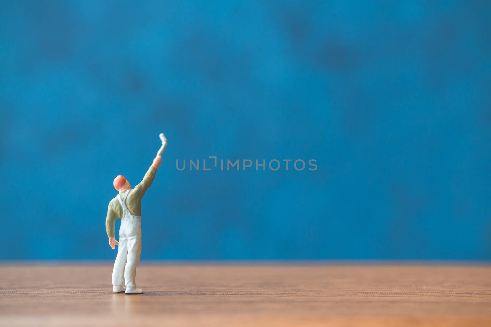 Miniature people holding brush in front of a blue wall background
