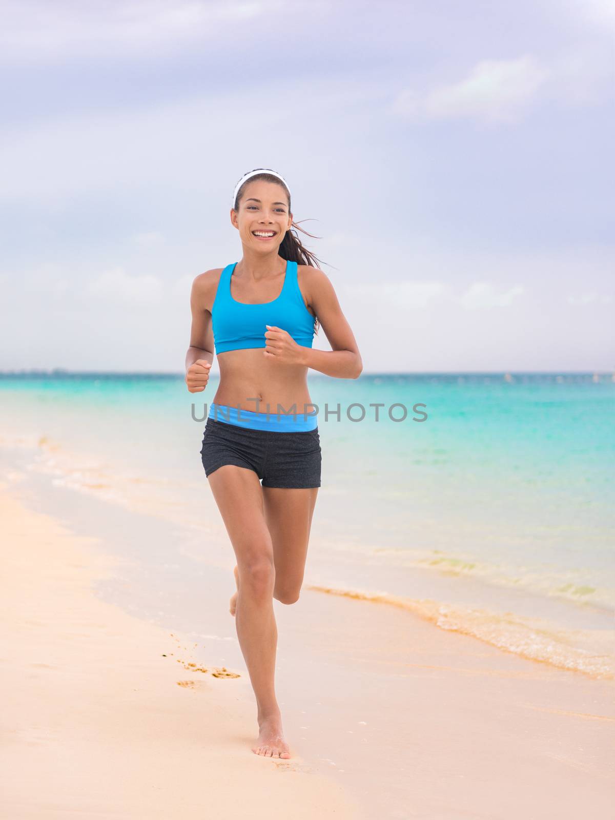 Active lifestyle young woman jogging on beach. Running barefoot on sand in Hawaii vacation travel Asian girl running on tropical holiday in blue activewear outfit.