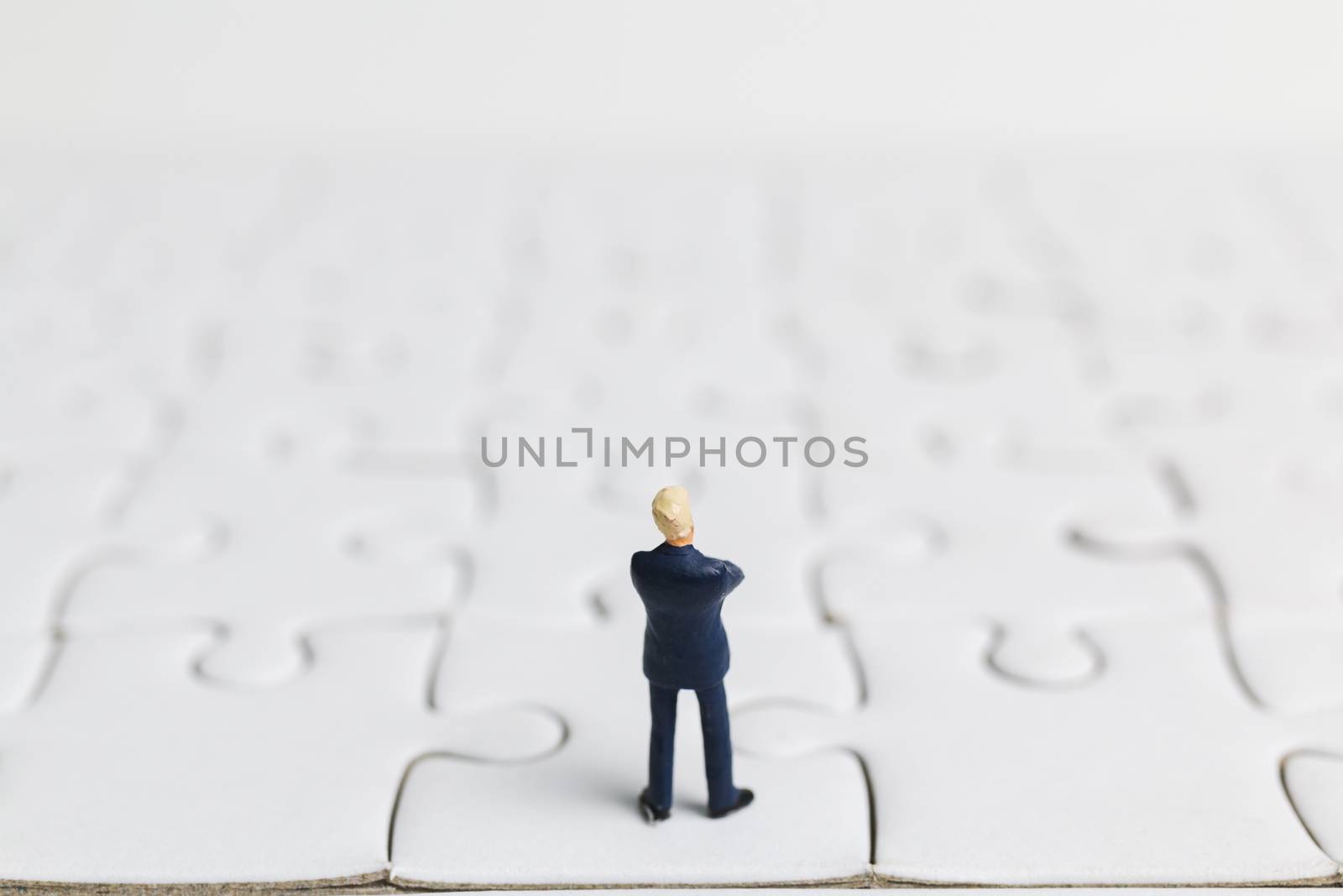 Miniature people: Businessman standing on white jigsaw. Business concept.
