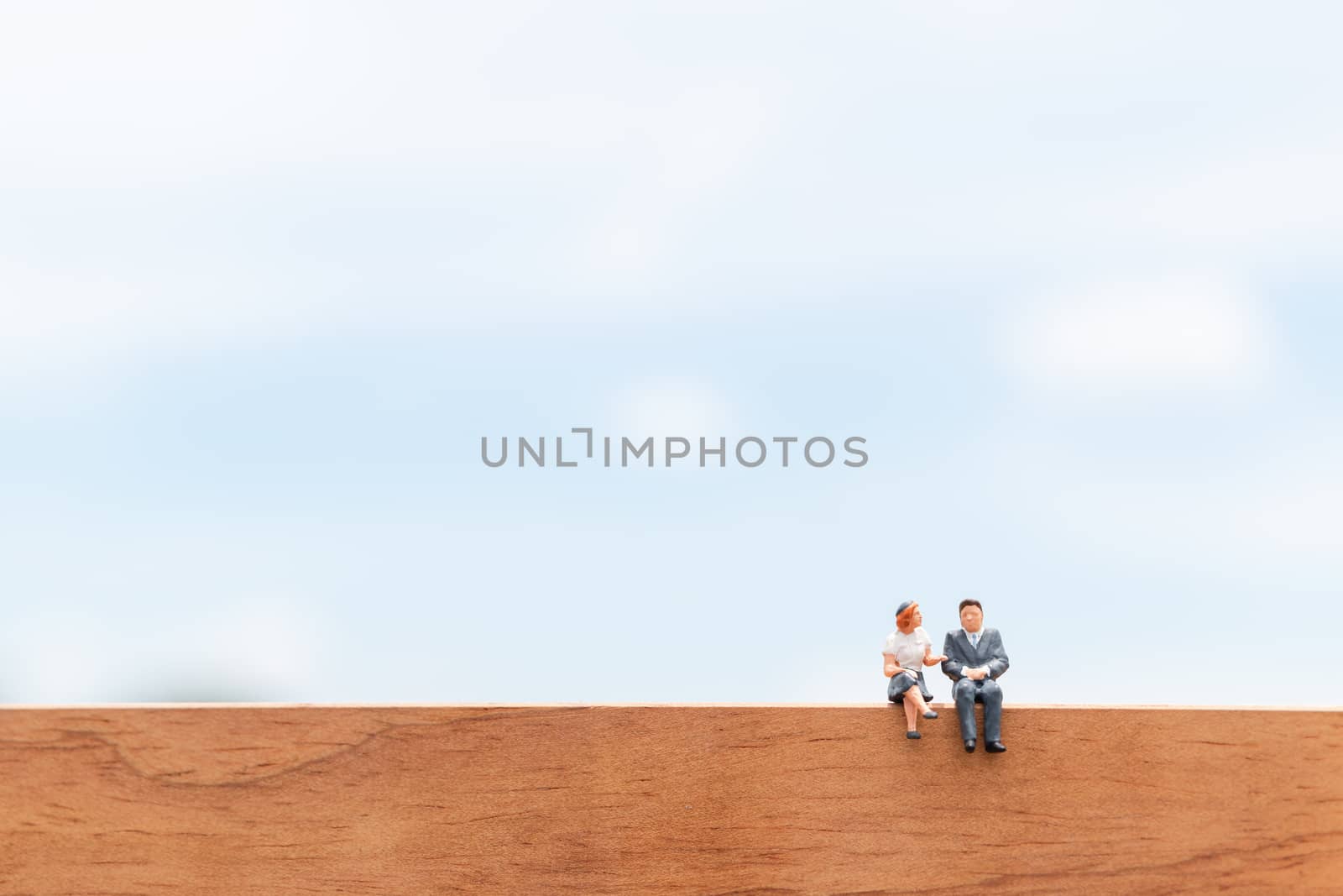 Miniature people:  Business people sitting on wooden floor with blue sky background