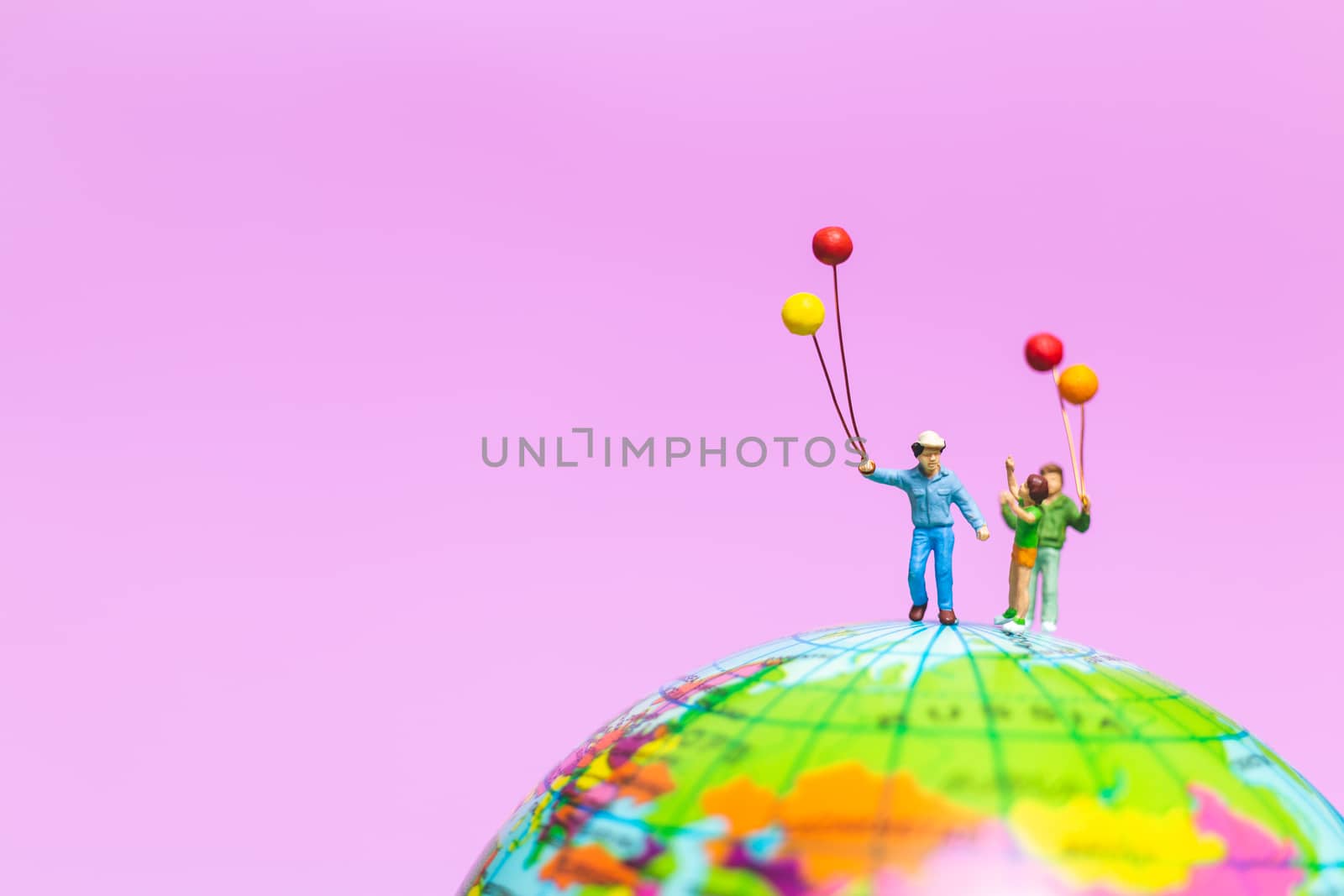 Miniature people : Happy family holding balloon on The globe with pink background and copy space for text