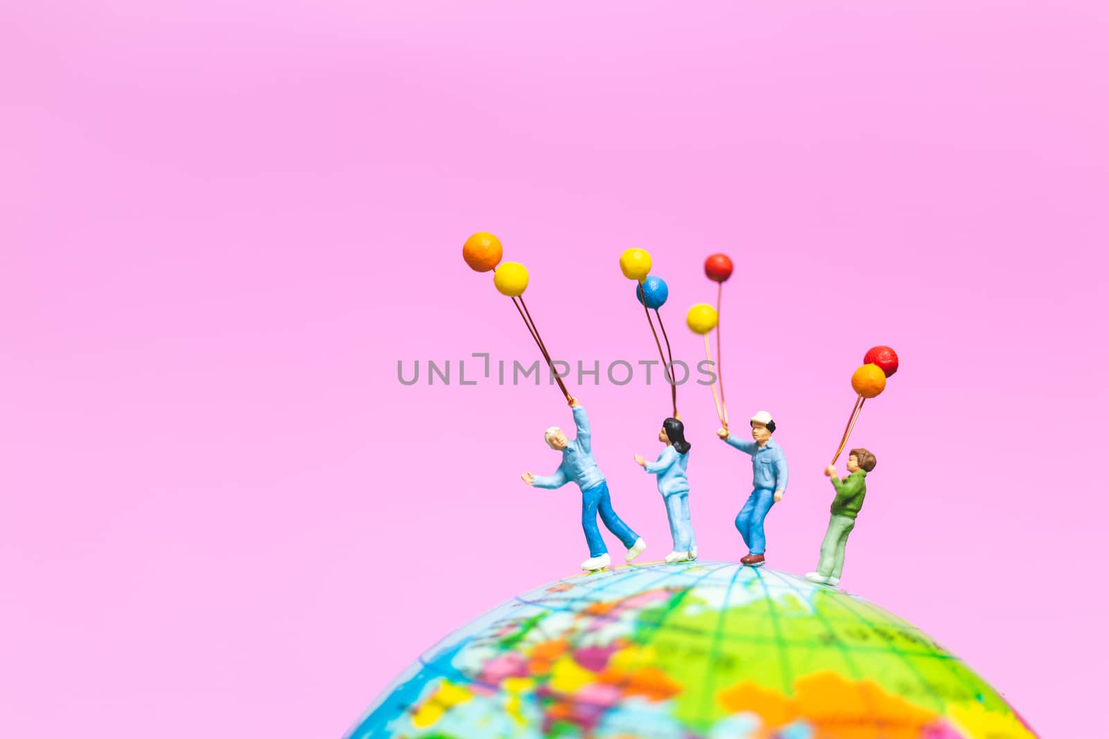 Miniature people : Happy family holding balloon on The globe with pink background and copy space for text