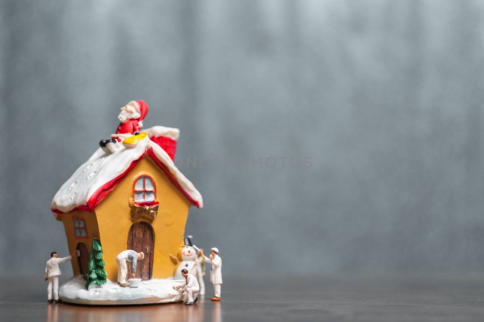 Miniature people painting house and Santa Claus sitting on the roof , Merry Christmas and happy holidays concept.