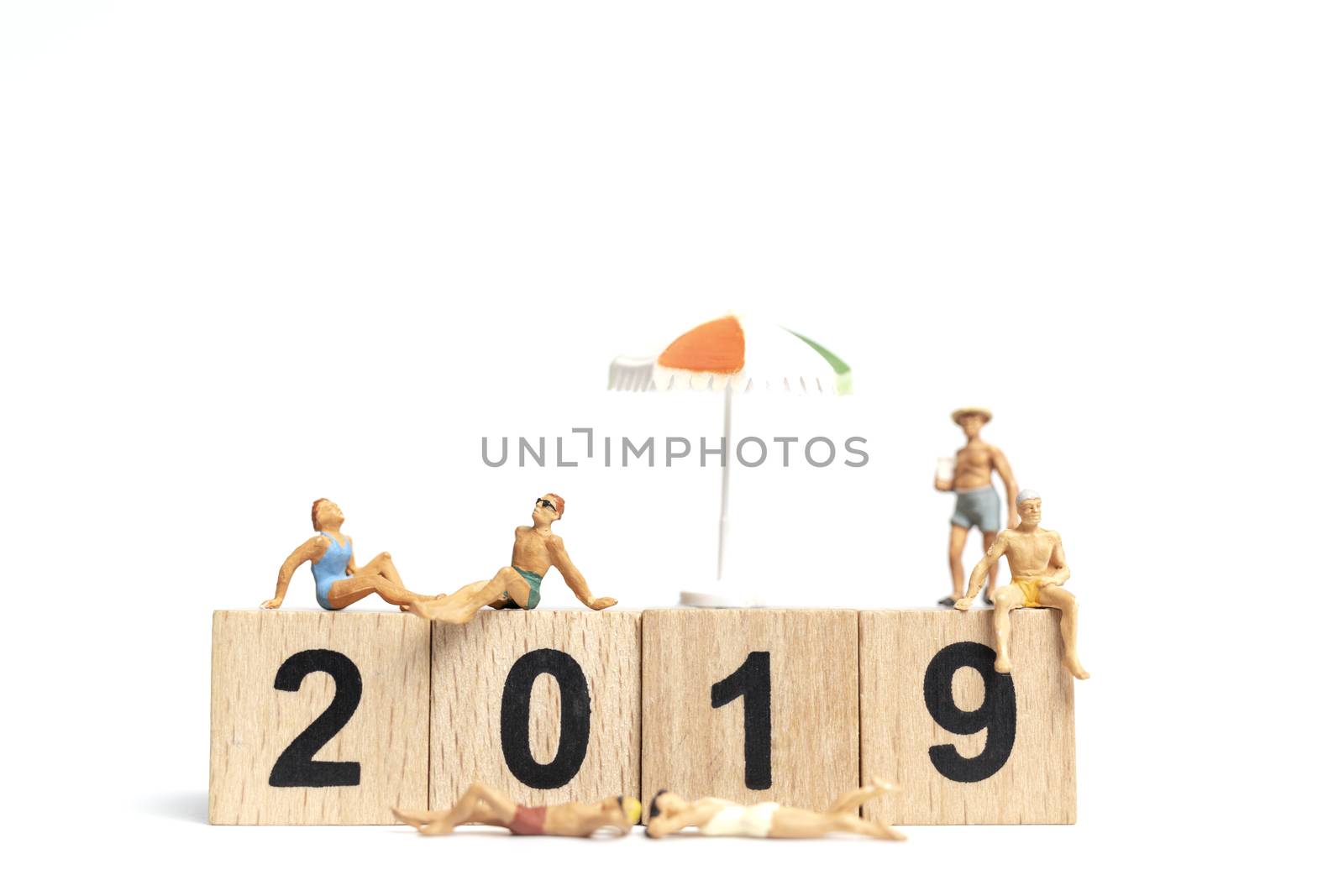 Miniature people wearing swimsuit relaxing on wooden block 2019 with white background
