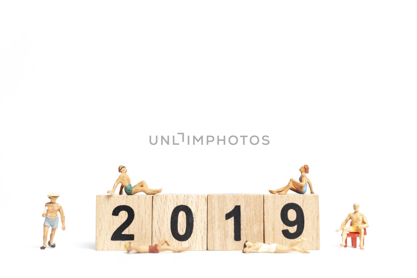 Miniature people wearing swimsuit relaxing on wooden block 2019 with white background