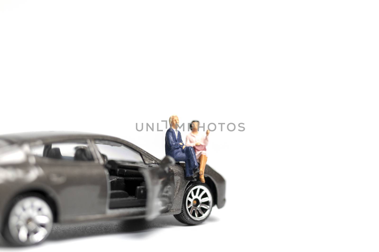 Miniature people sitting on car with copy space on white background 