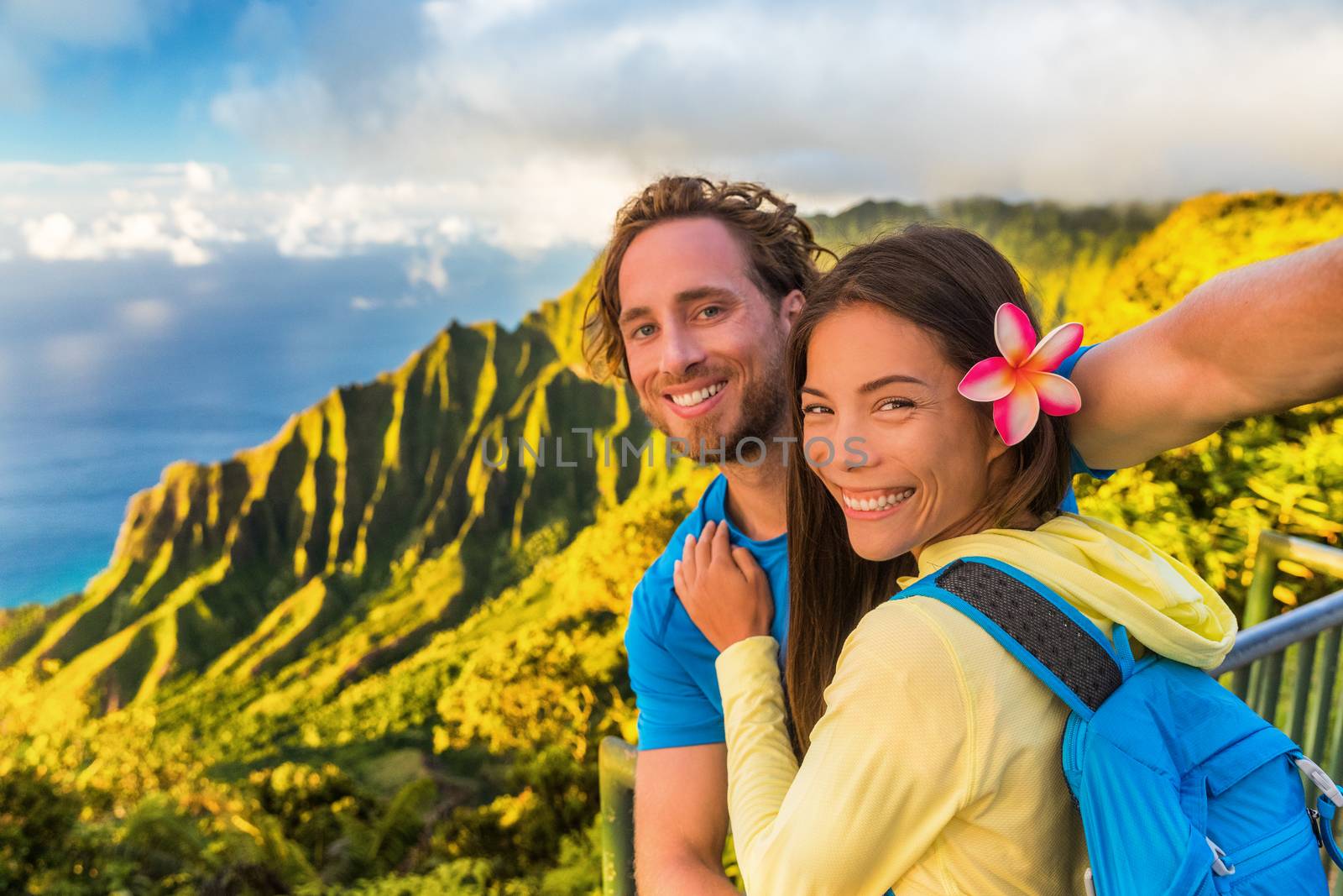 Na pali hikers couple tourists taking selfie at Napali lookout in Kauai Hawaii. Travel friends taking smartphone picture at famous destination Kalalau hawaiian attraction by Maridav