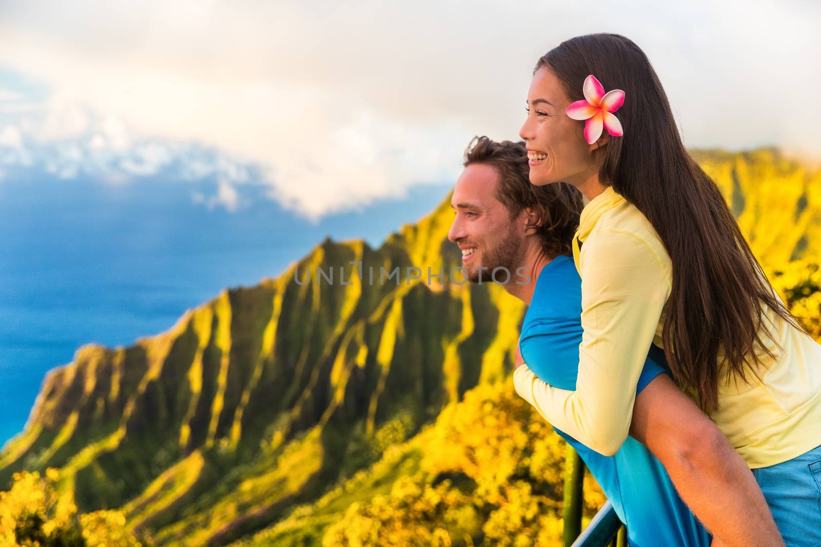 Travel couple fun piggyback at Na Pali Kauai Hawaii vacation adventure. Happy young Asian woman and Caucasian man piggybacking at nature lookout in mountains sunset. Love honeymoon vacations by Maridav