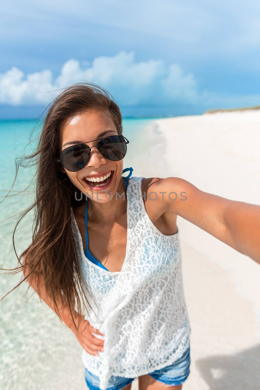 Beach selfie young Asian woman taking fun photo with phone on Caribbean tropical summer holidays. Girl wearing sunglasses.