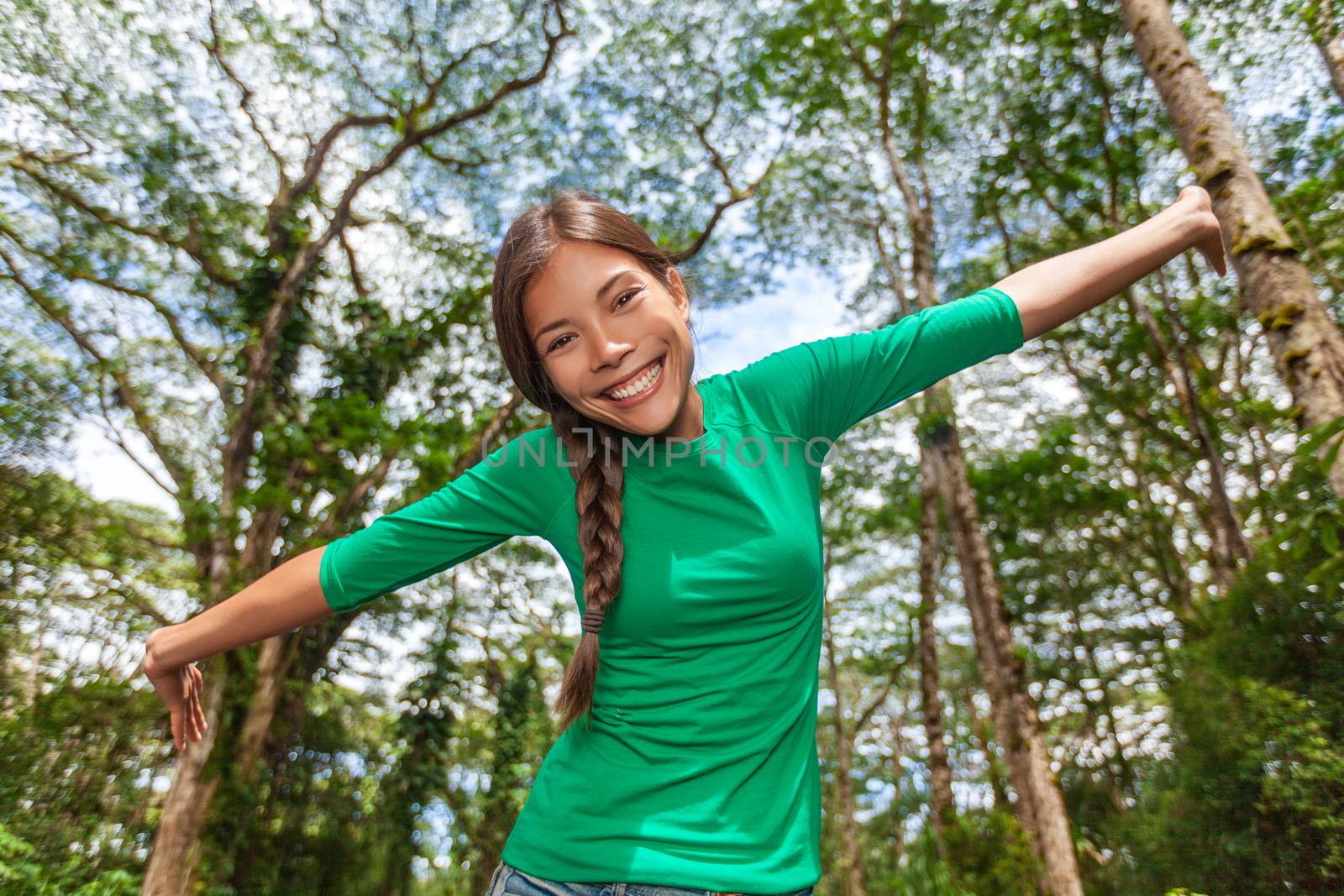 Environment friendly happy girl enjoying nature forest outdoors in natural sunny background. Asian woman with open arms in freedom having fun in fresh air, tall green trees.