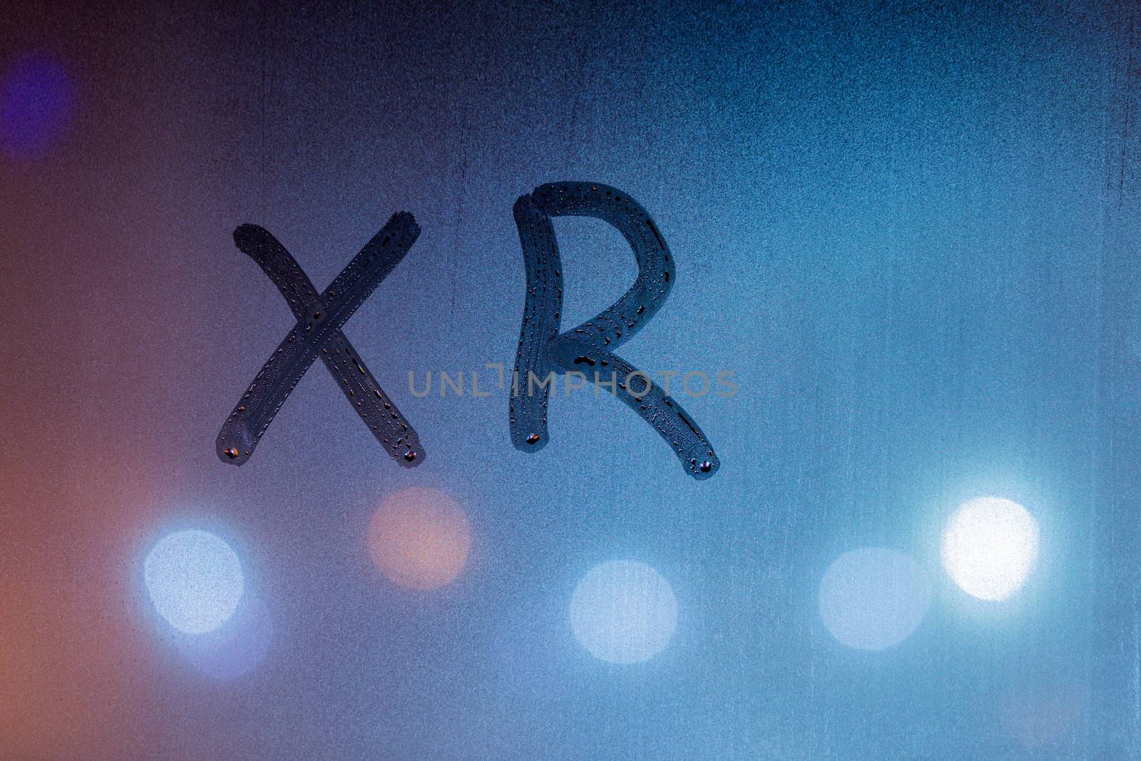 an abbreviation xr for extended reality handwritten on blue night wet window glass.