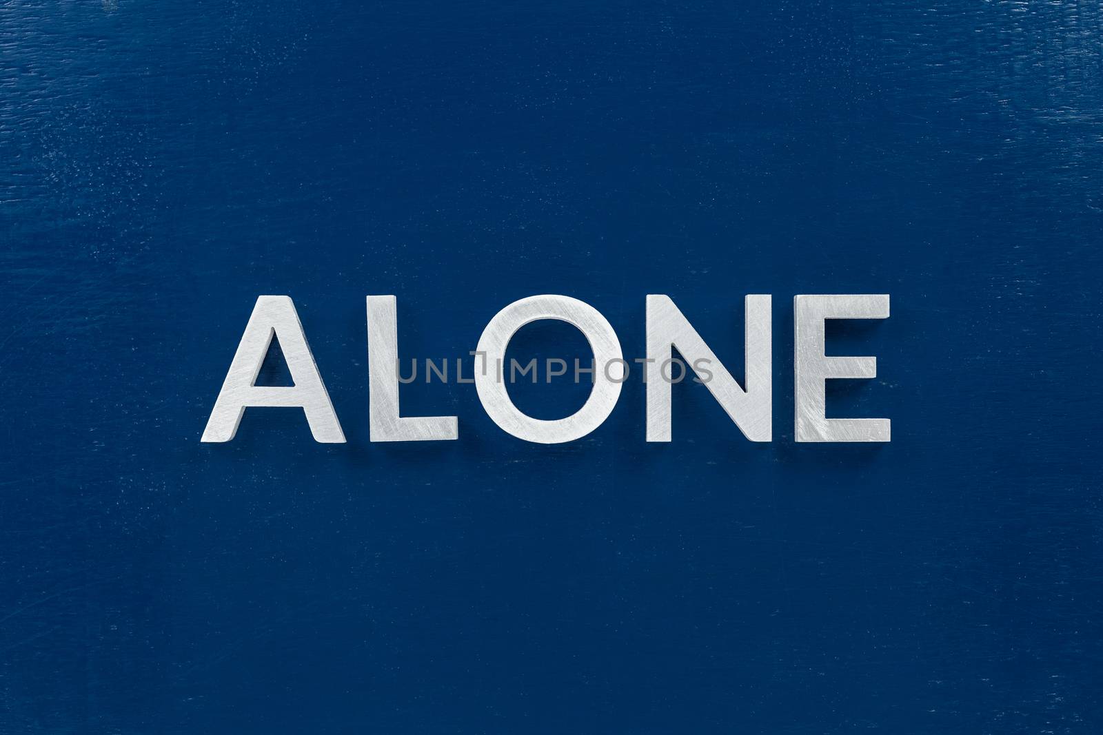 The word alone laid with silver metal letters in center of painted classic blue flat board. View in flat lay perspective. by z1b