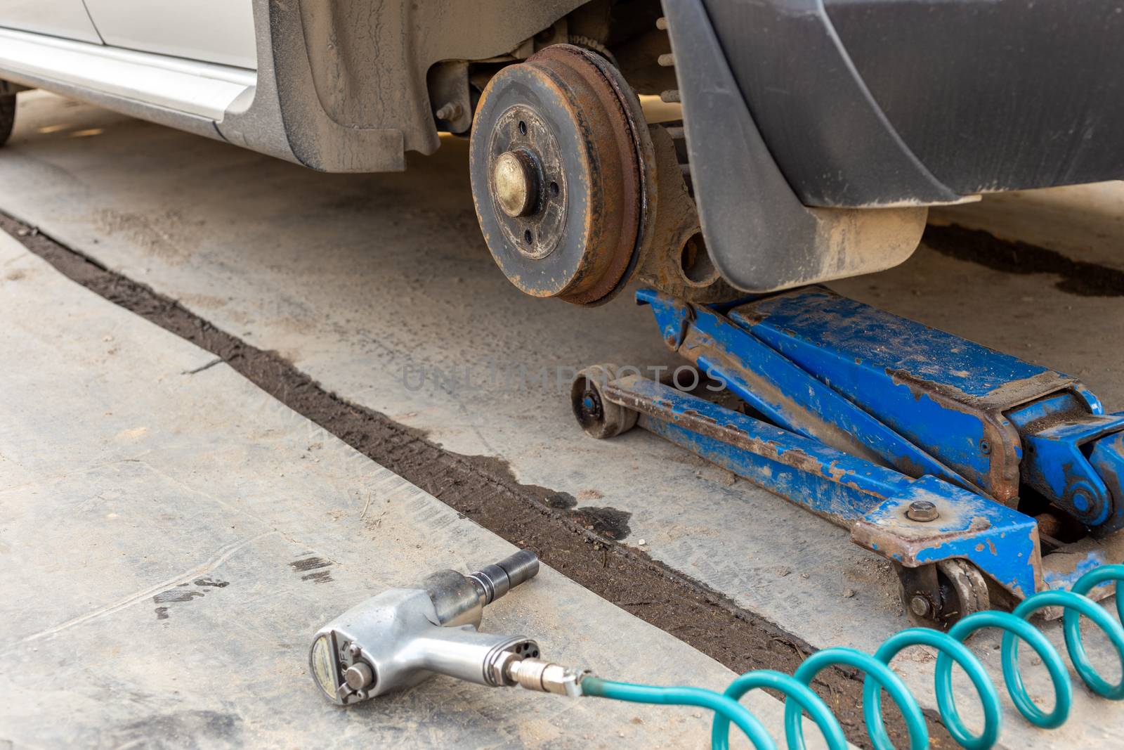 Car without wheel lifted with hydraulic floor jack and pneumatic impact wrench in a outdoors car workshop. Season tire changing procedure. Close view with selective focus and background blur.