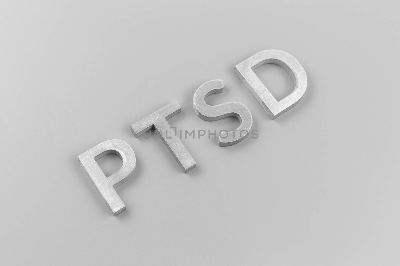 an abbreviation PTSD - post traumatic stress disorder - laid with silver metal letters on light grey flat surface in ascending diagonal composition