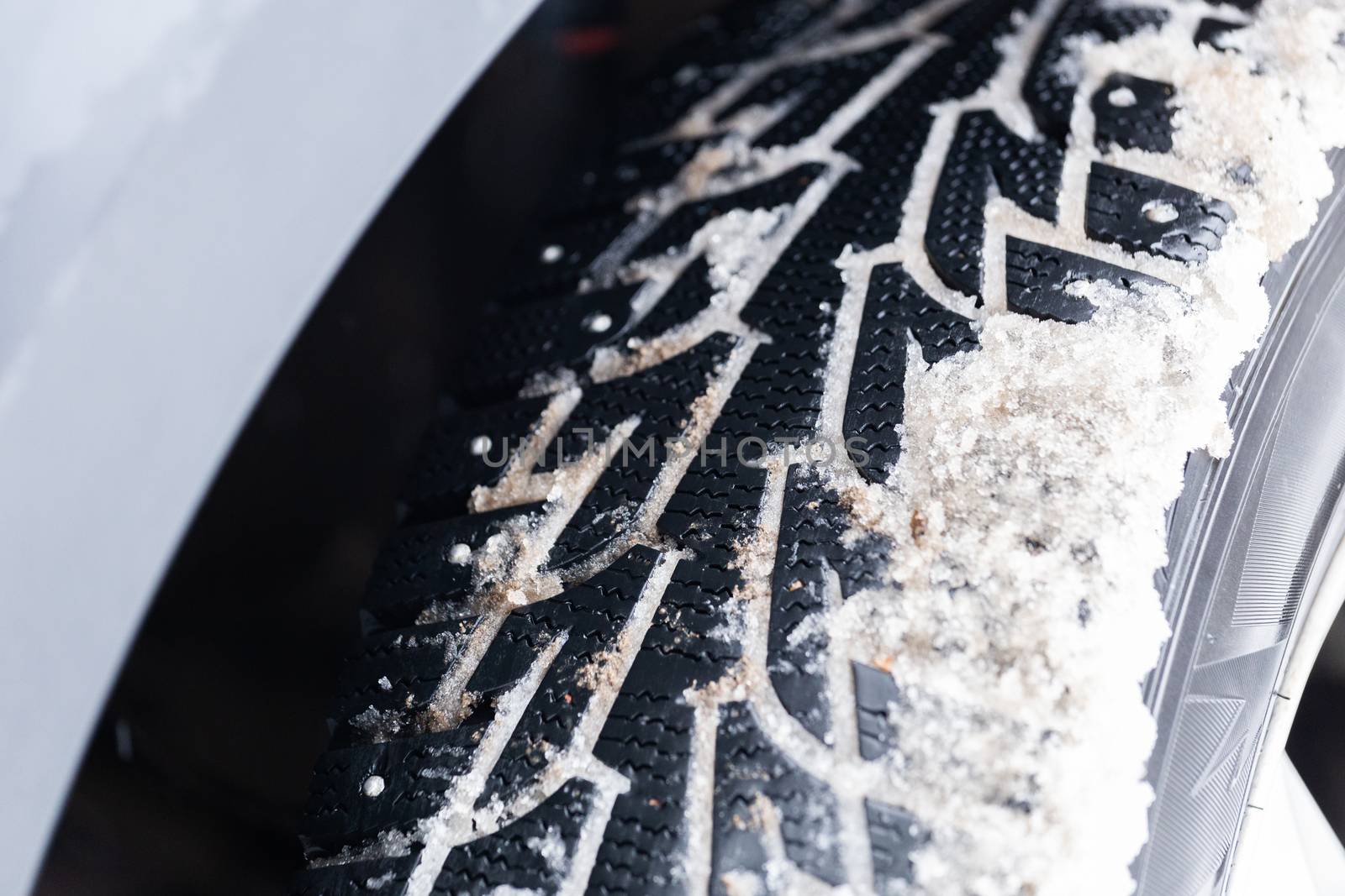 an unadorned picture of winter car wheel with metal spikes on snow close-up.