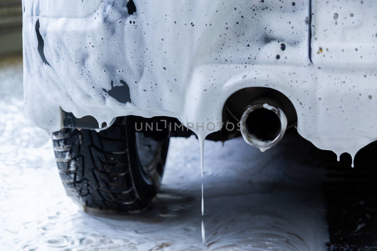 a fossil fuel car covered by soap foam while washing indoors - close-up low angle view from back with selective focus.