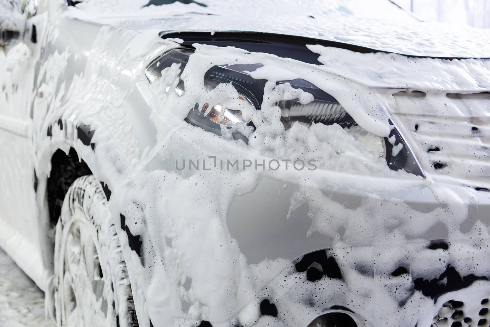 a car covered by soap foam while washing indoors - close-up wiew with selective focus.