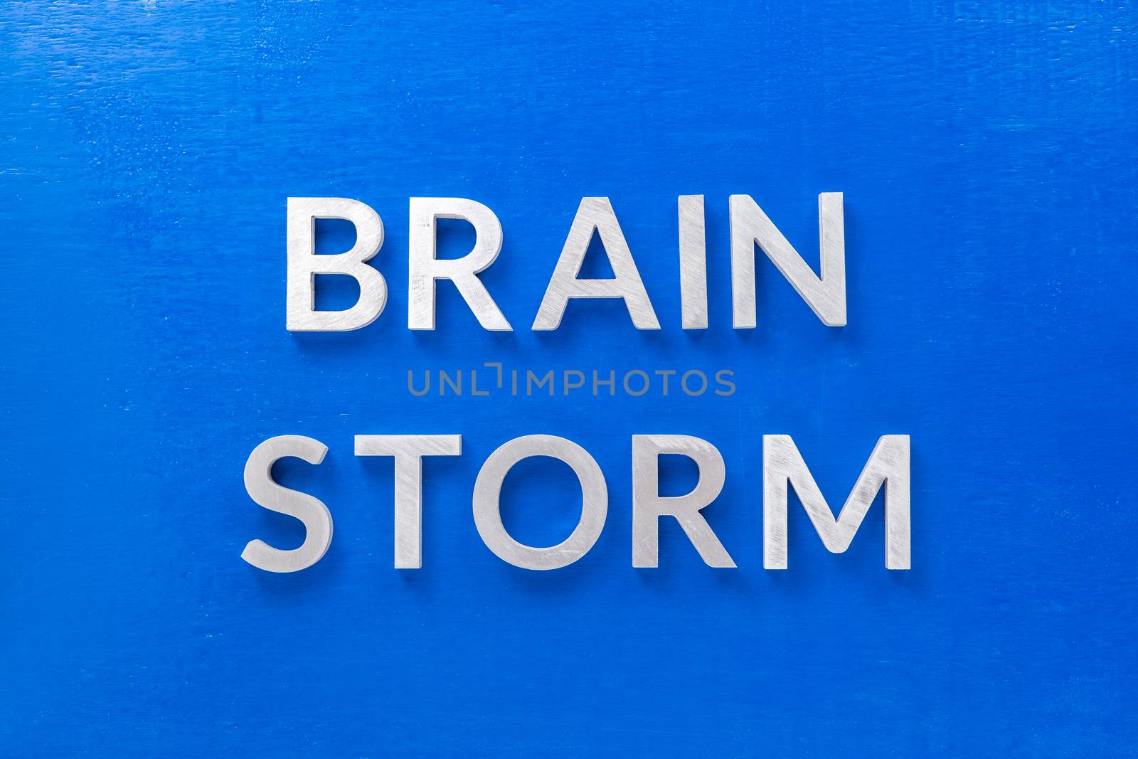 the phrase brain storm laid with silver metal letters on blue board in flat lay with central composition.