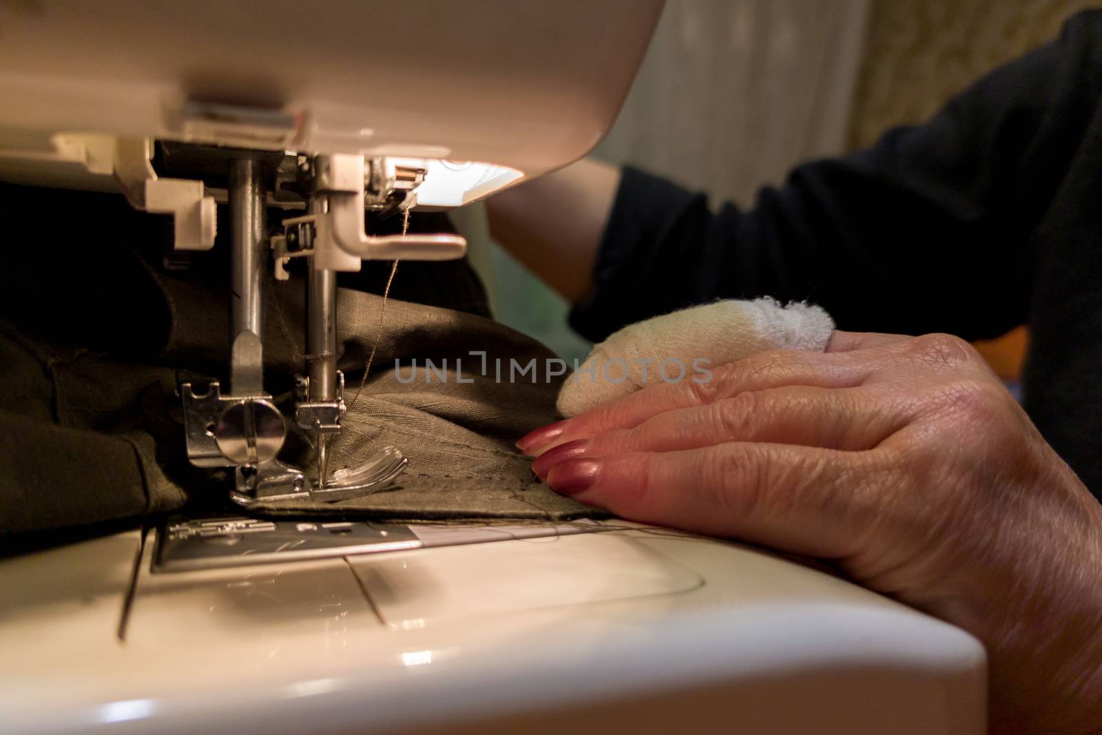 a hand of aged womans with a bandaged finger sews with a sewing machine by z1b