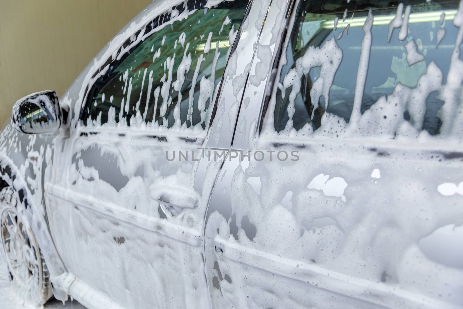 a car covered by soap foam while washing indoors - close-up with selective focus.