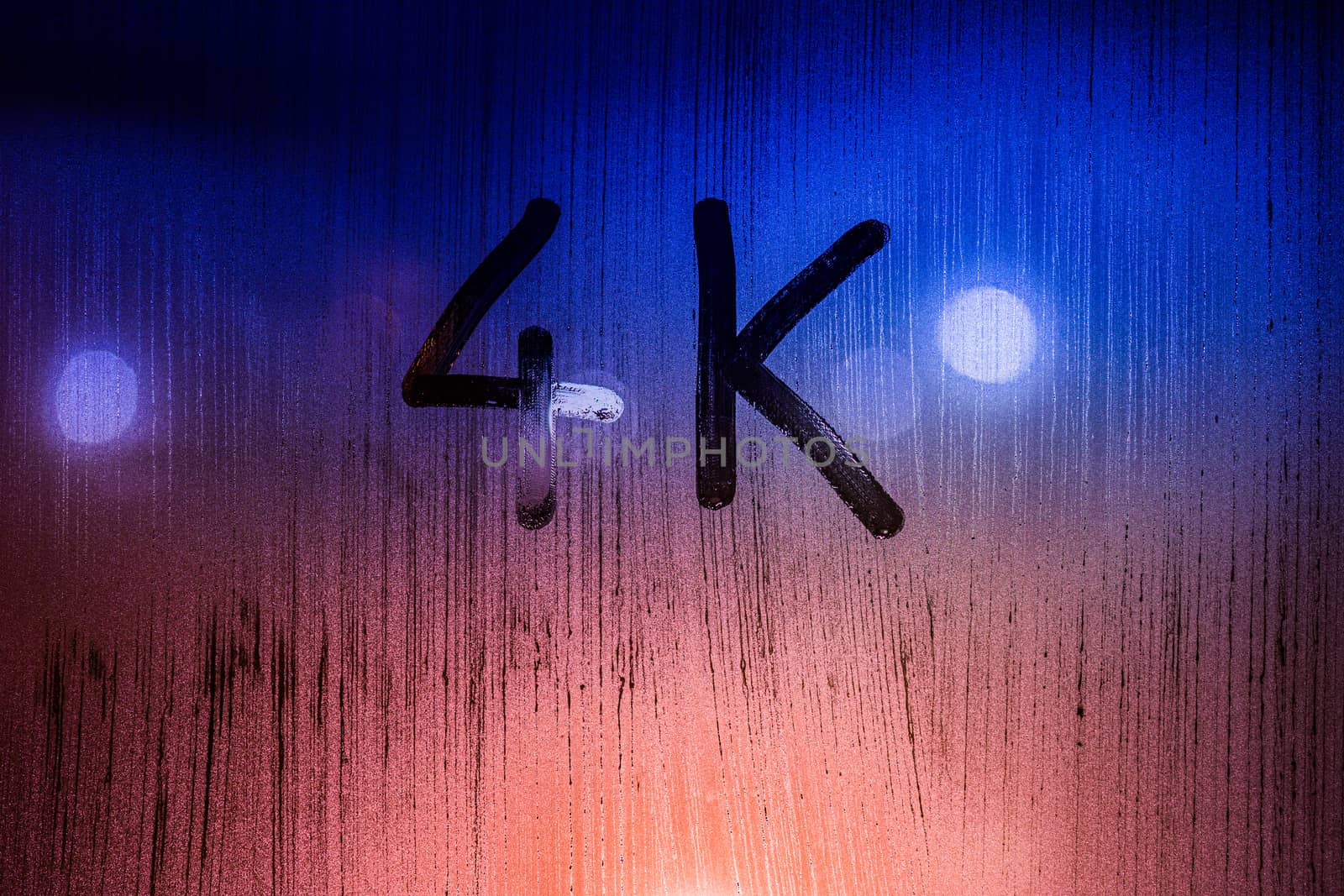 The word 4k handwritten on wet glass with blurred night lights in background.