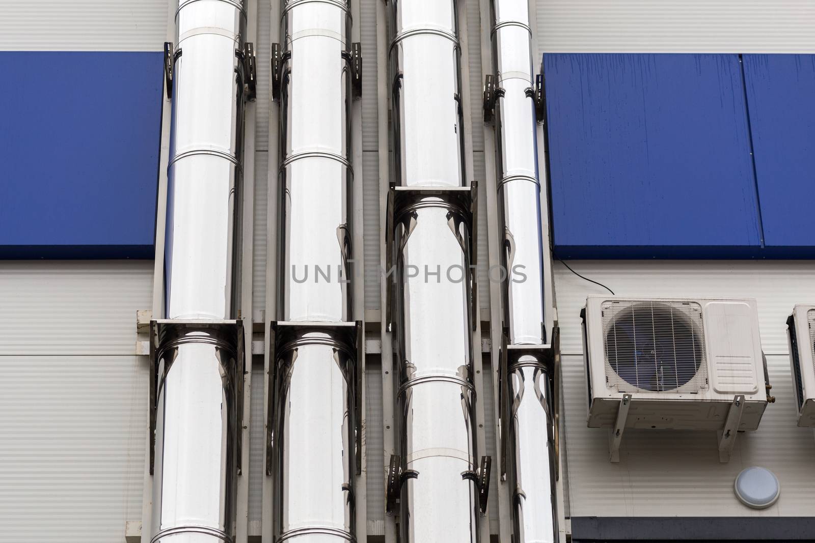 Chrome ventilation pipes on the outside wall of the white and blue Industrial building.