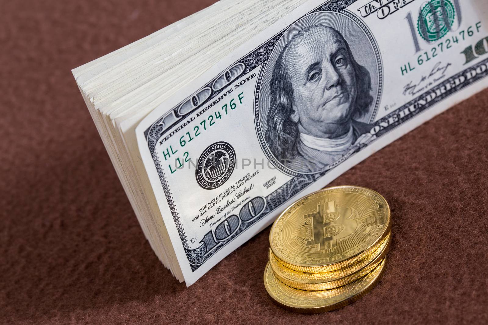 a bunch of us dollar banknotes and three bitcoin shiners on brown fleece background close-up with selective focus.