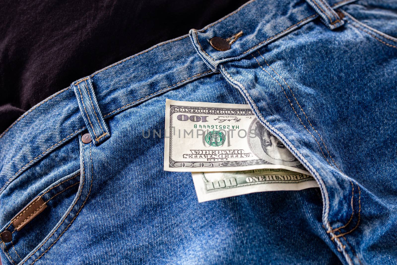 a two hundred dollar bills inside codpiece of blue jeans close-up with selective focus.