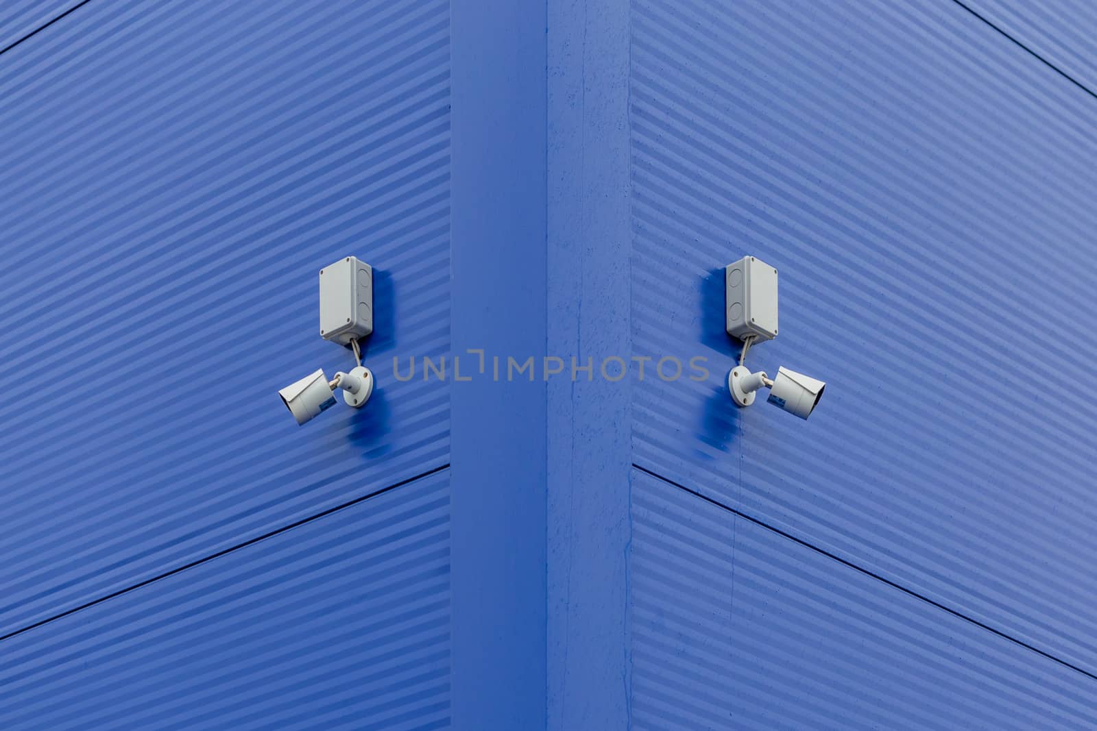 two small white security cameras on blue steel building corner.