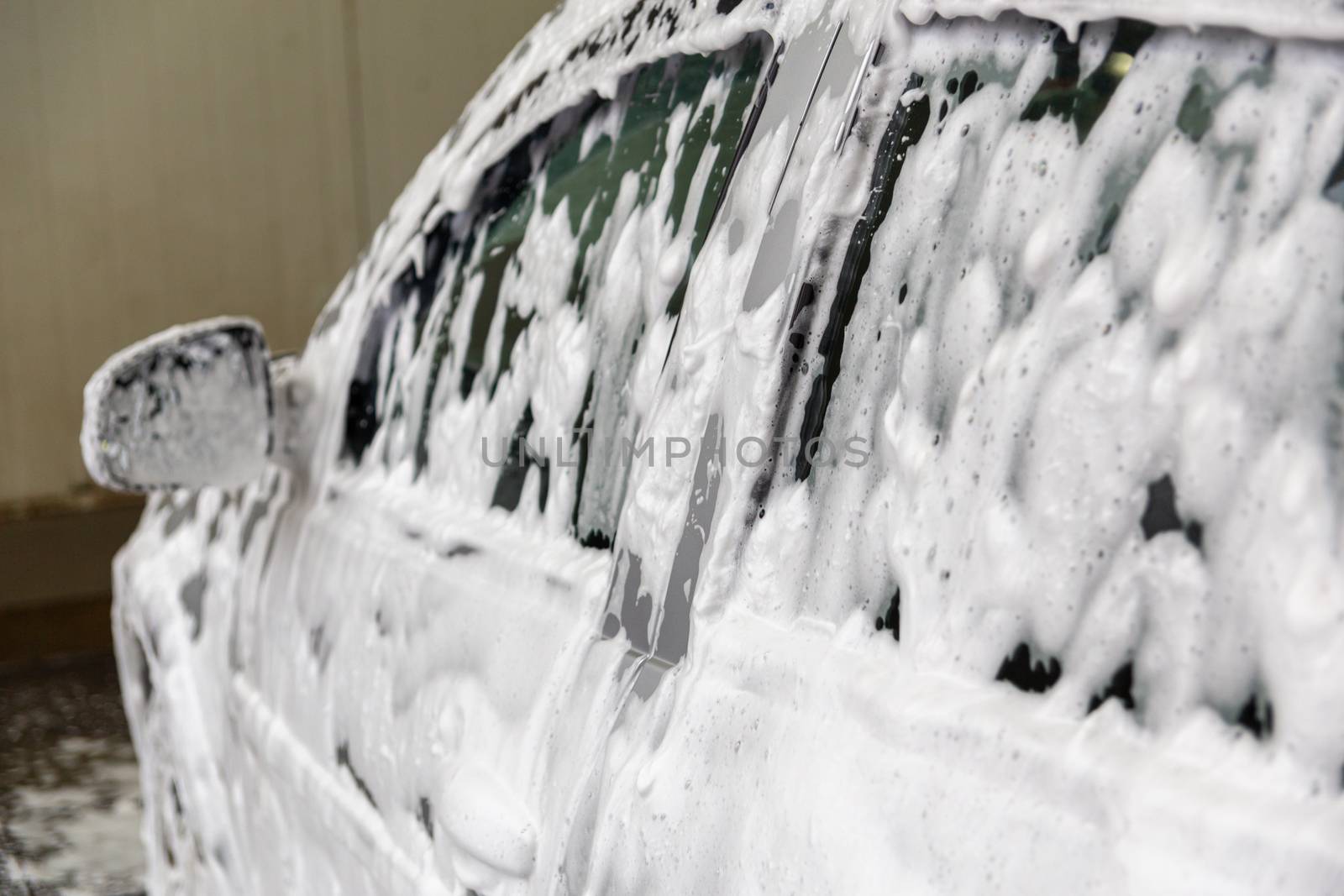 a car covered by soap foam while washing indoors - close-up with selective focus.