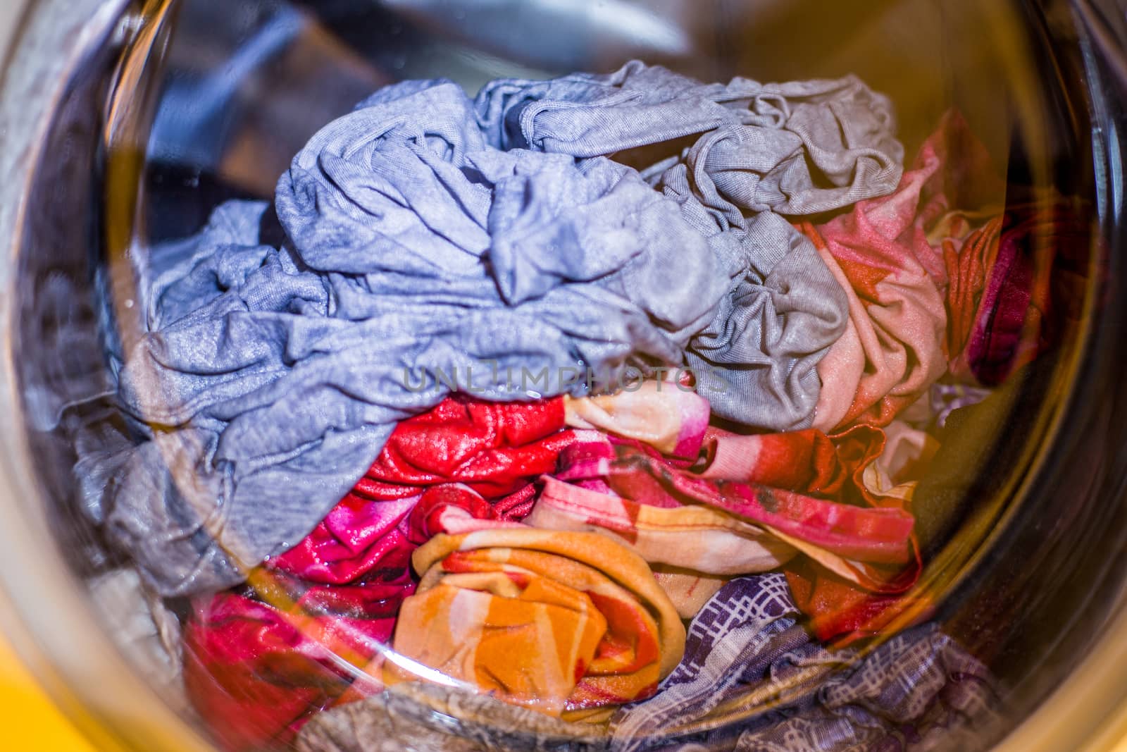 a close view of domestic washing machine at work with wet colored cloth inside.
