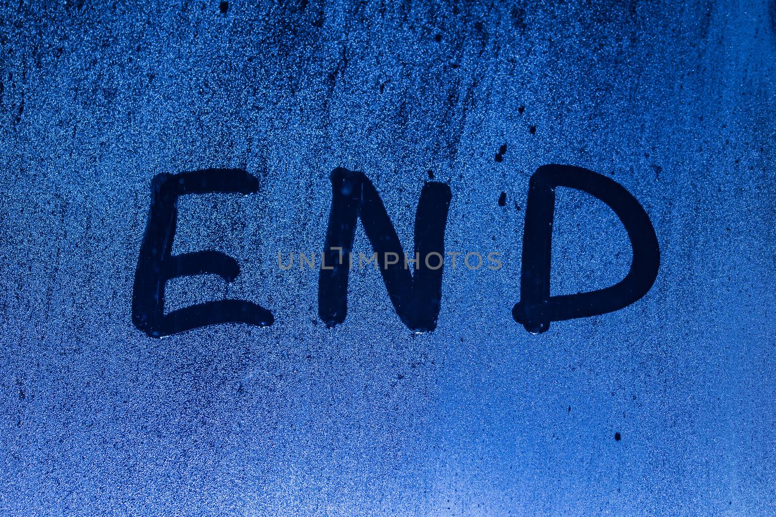 The word end written on night sweaty window glass with blurred blue light in the background.