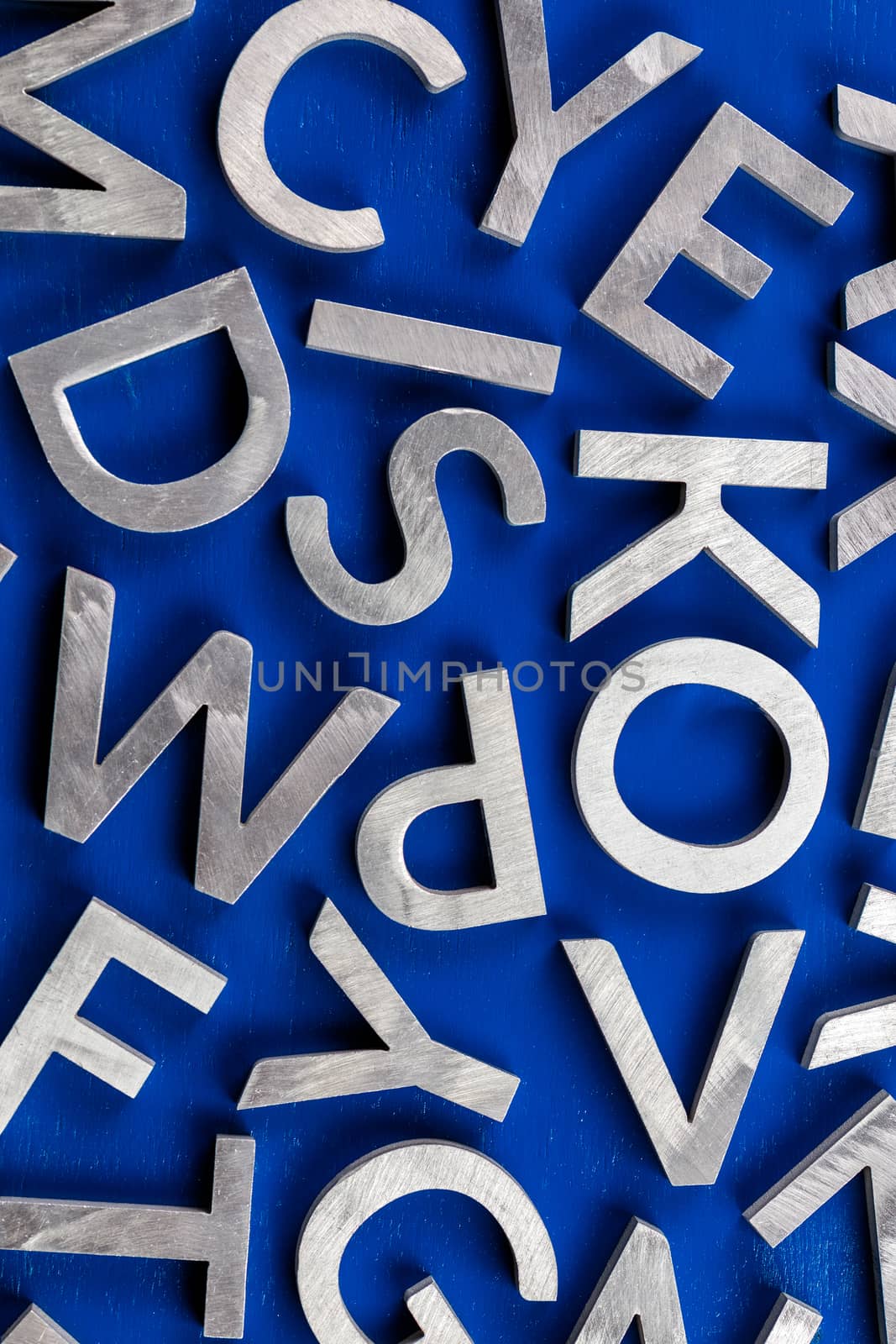 Abstract flat background of silver metal english alphabet characters on blue background. Flat lay abstraction for back to school or language education concept.