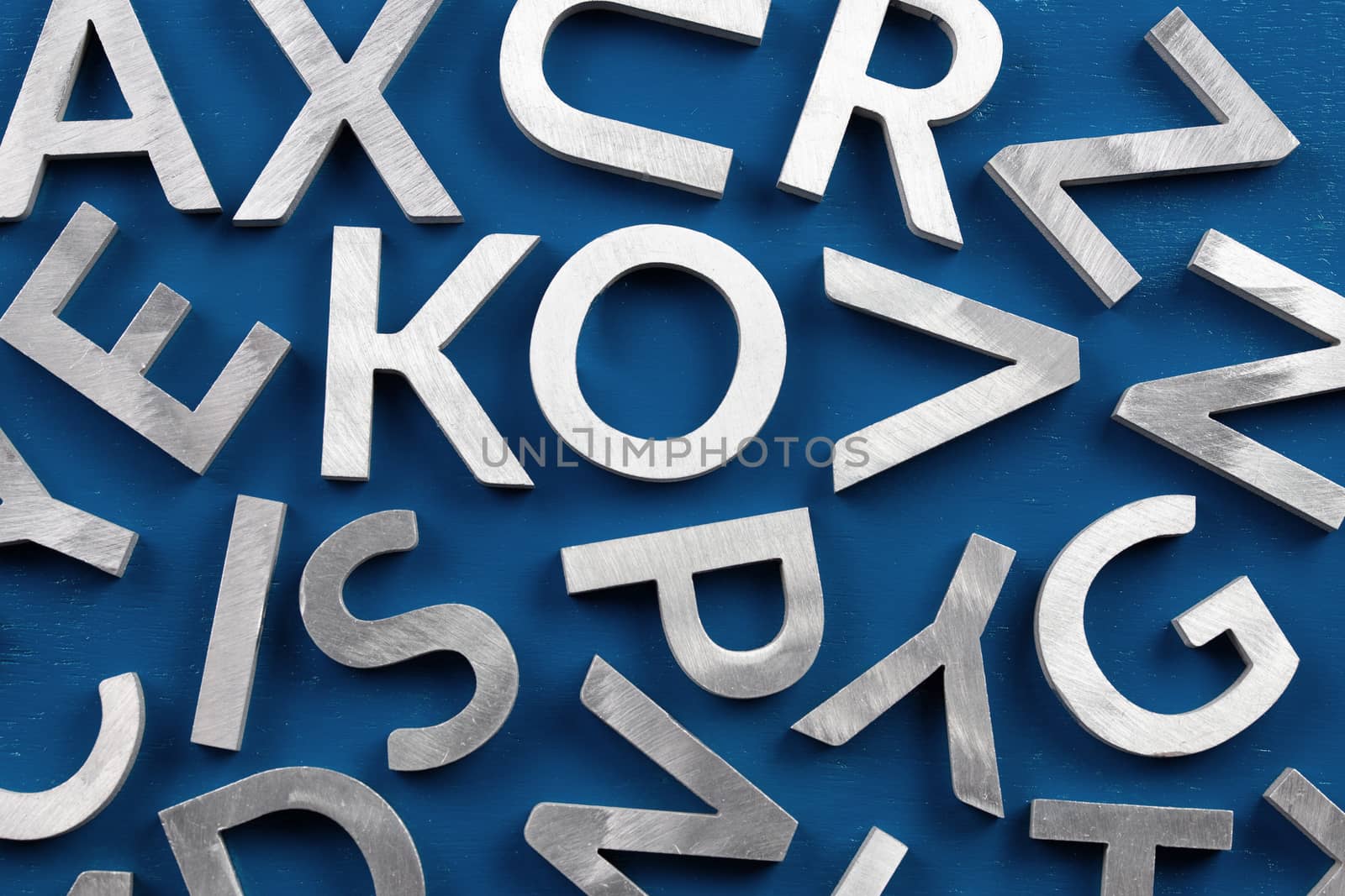 Abstract flat background of silver metal english alphabet characters on classic blue background. Flat lay abstraction for back to school or language education concept.