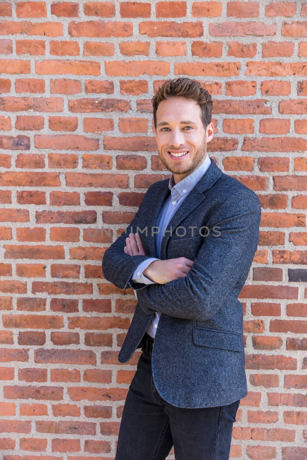 Businessman portrait on brick wall background. Young confident smiling man standing arms crossed, looking at camera.