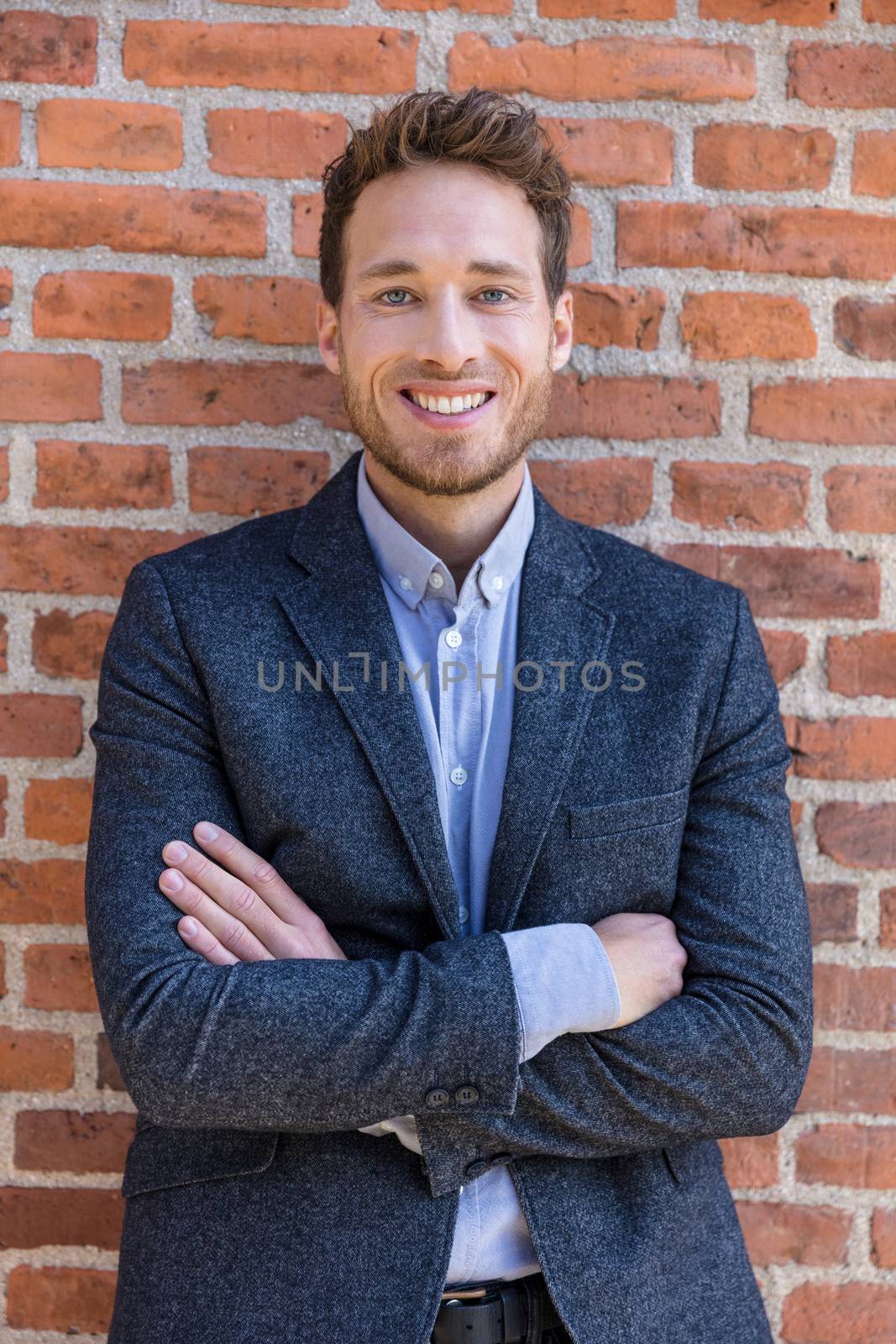 Happy smart casual businessman portrait on urban city brick wall background lifestyle portrait. Young professional man smiling confident in blazer. Career and entrepreneurship concept.