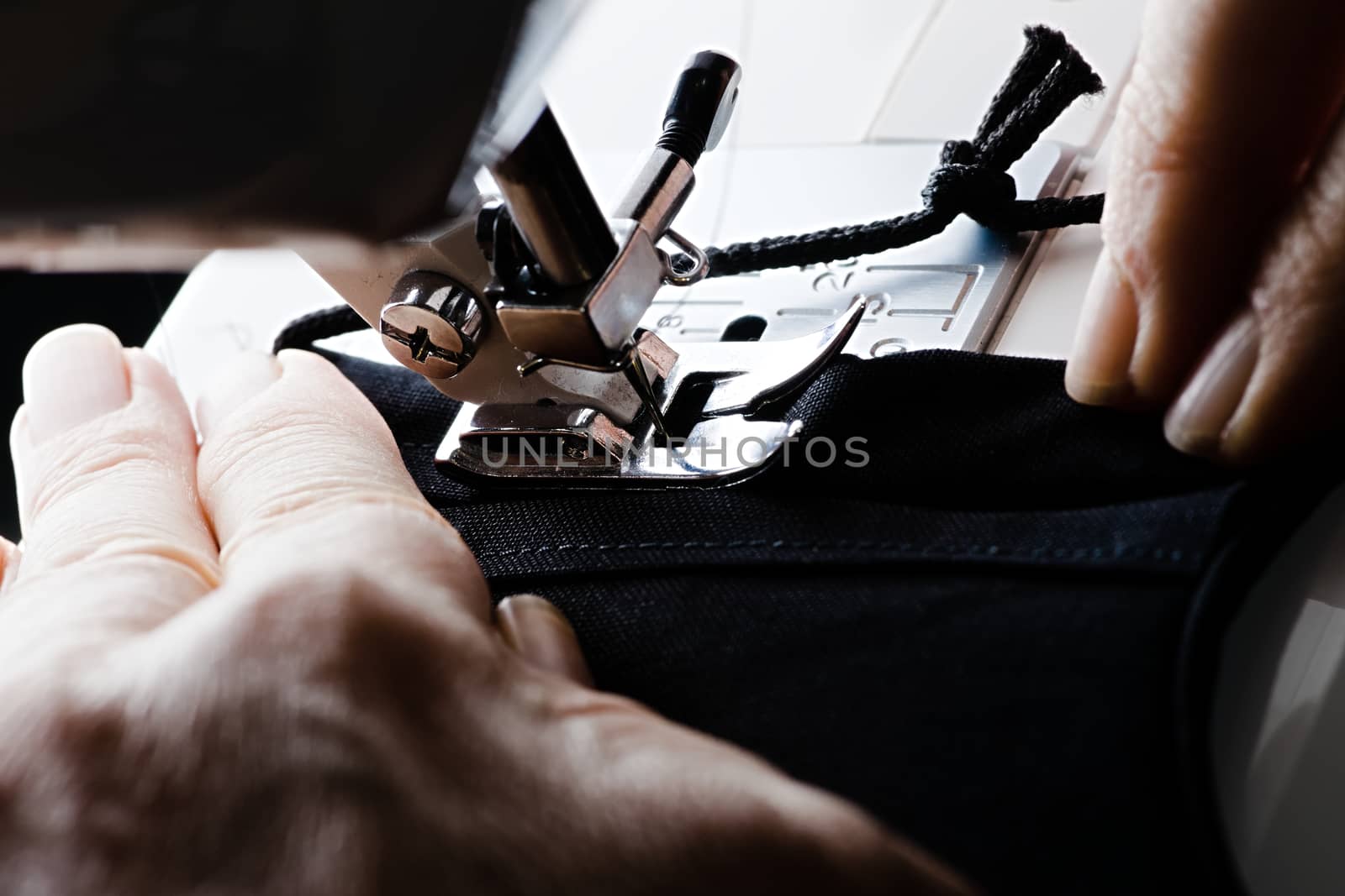 From right to left, a seam is stitched on a black homemade face covering or face mask. Guided by older weathered hands.