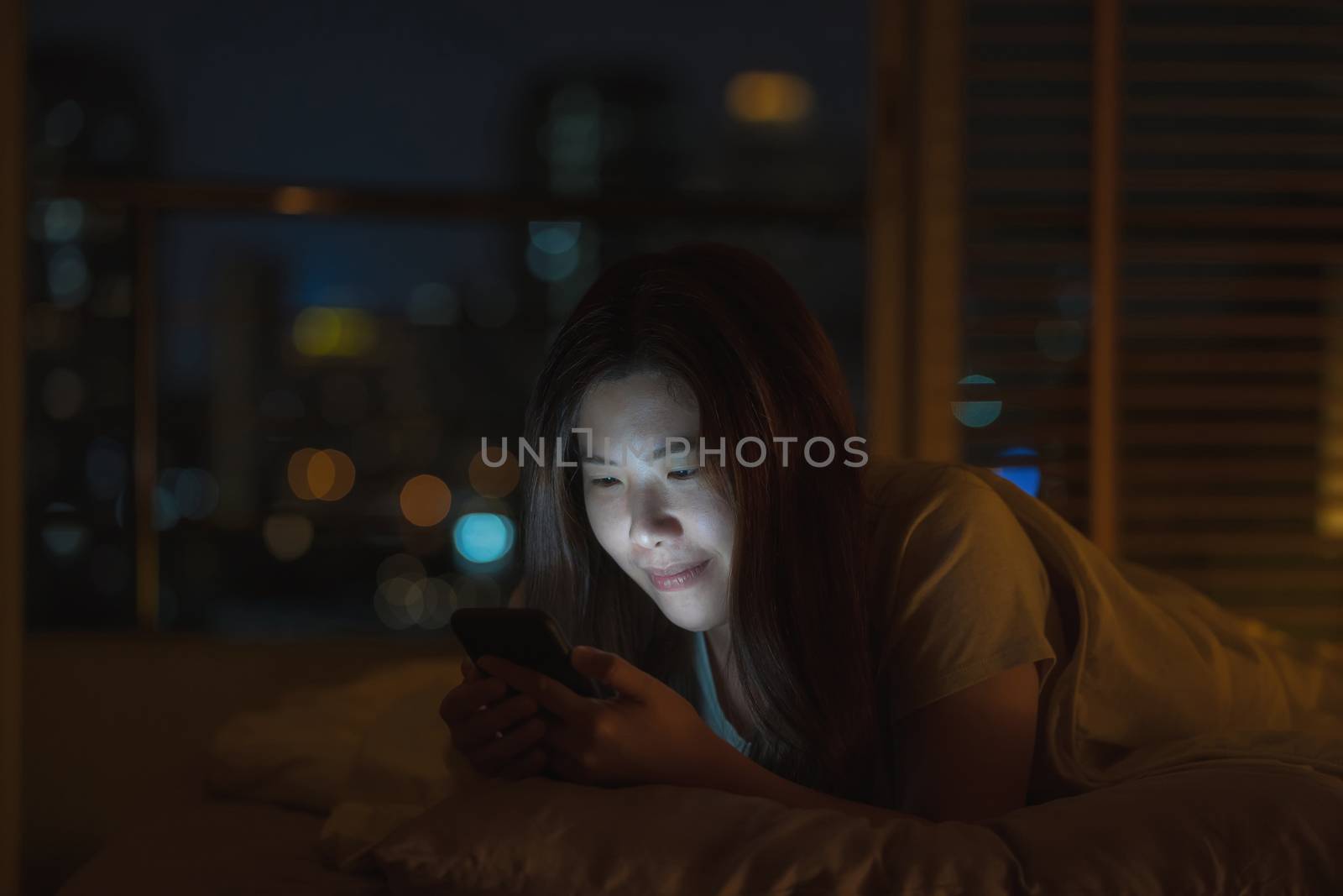 Asian woman sleeping and using smart mobile phone for social network or video conference call when Covid19 Outbreak,  quarantine, and Coronavirus pandemic, Social distancing and new normal concept